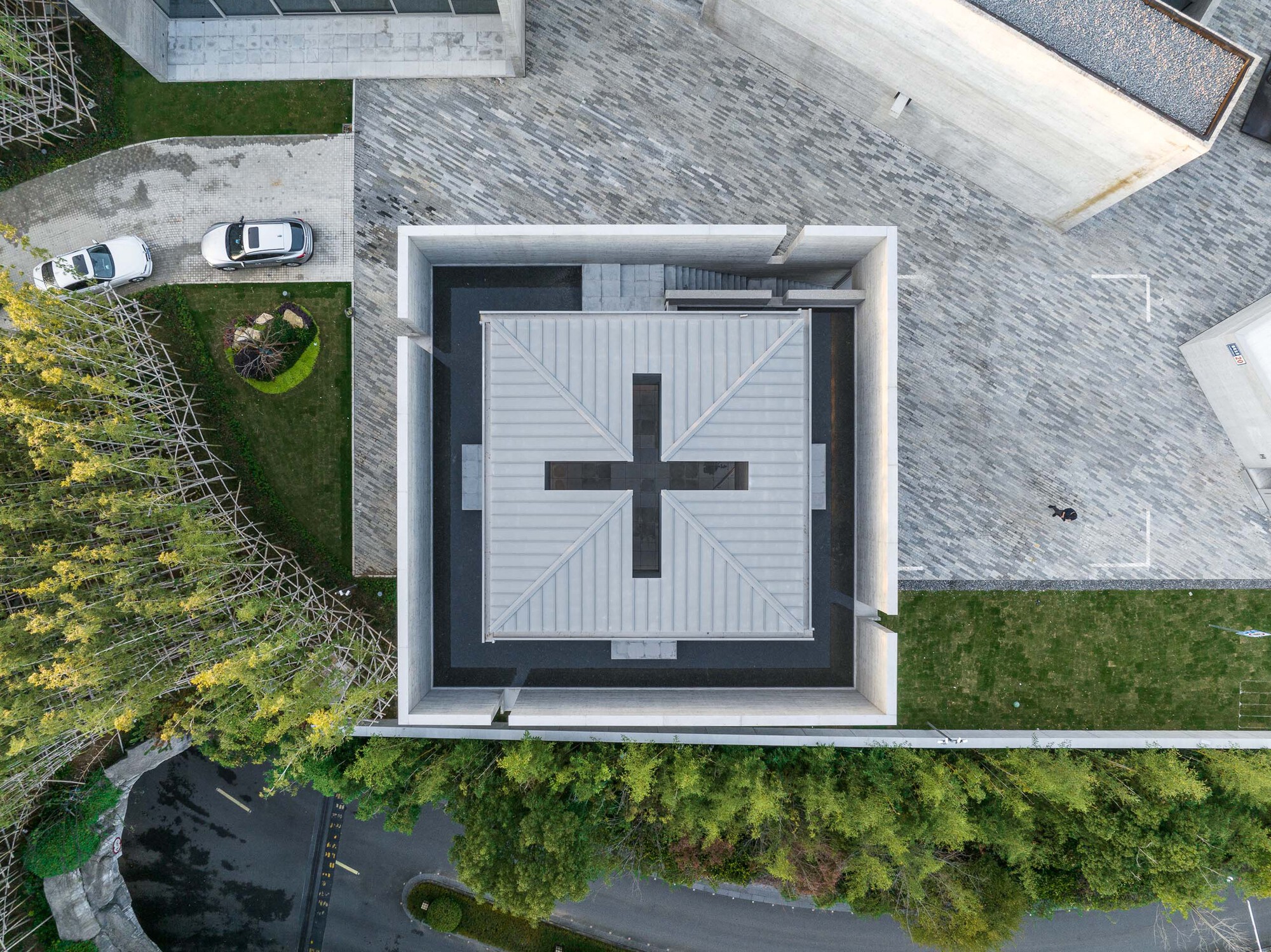 Top-down view of cruciform skylight with white metal cladding set within dark framed courtyard