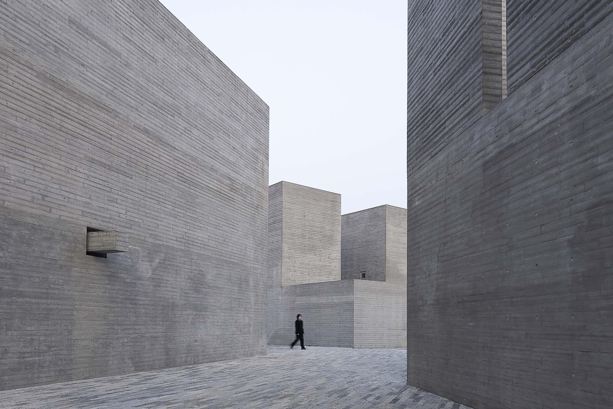Narrow courtyard between stepped concrete block walls with a single figure walking through the space