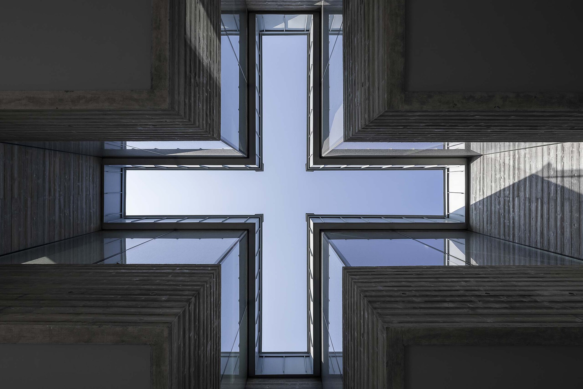 Cruciform skylight framed by board-formed concrete walls and glass panes against blue sky