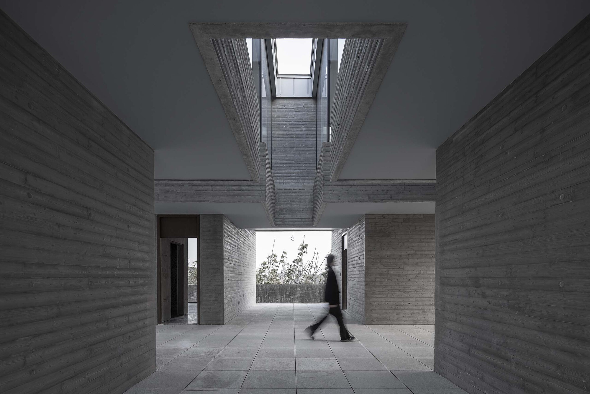 Interior courtyard with board-formed concrete walls, open skylight above, and a person in motion