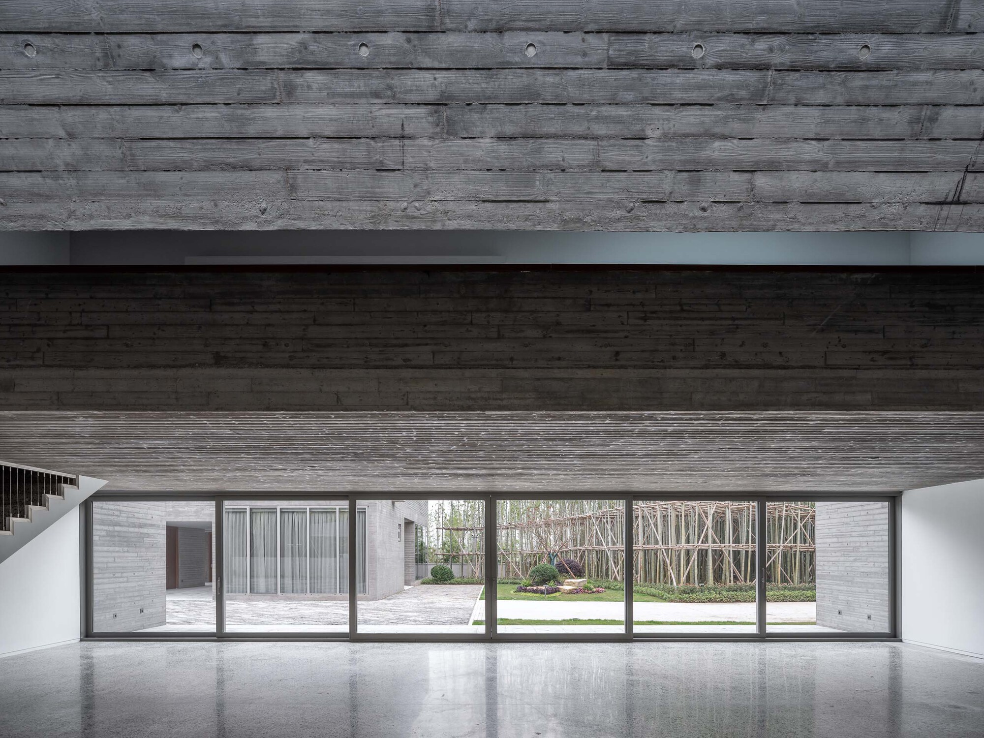 Interior with horizontal timber ceiling and floor-to-ceiling glazing overlooking a courtyard and birch grove