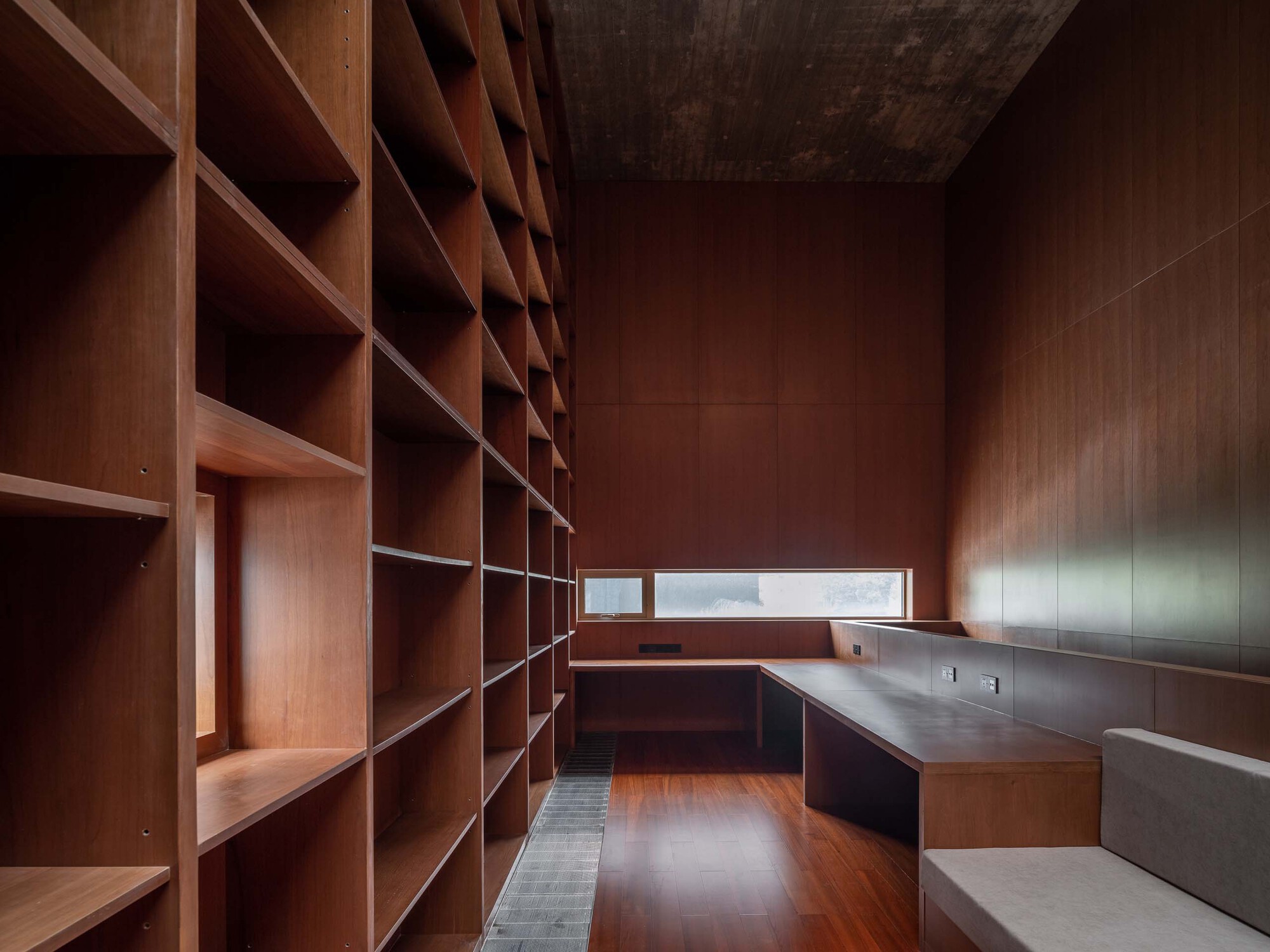 Wood-paneled library room with built-in shelving and a horizontal window admitting soft daylight