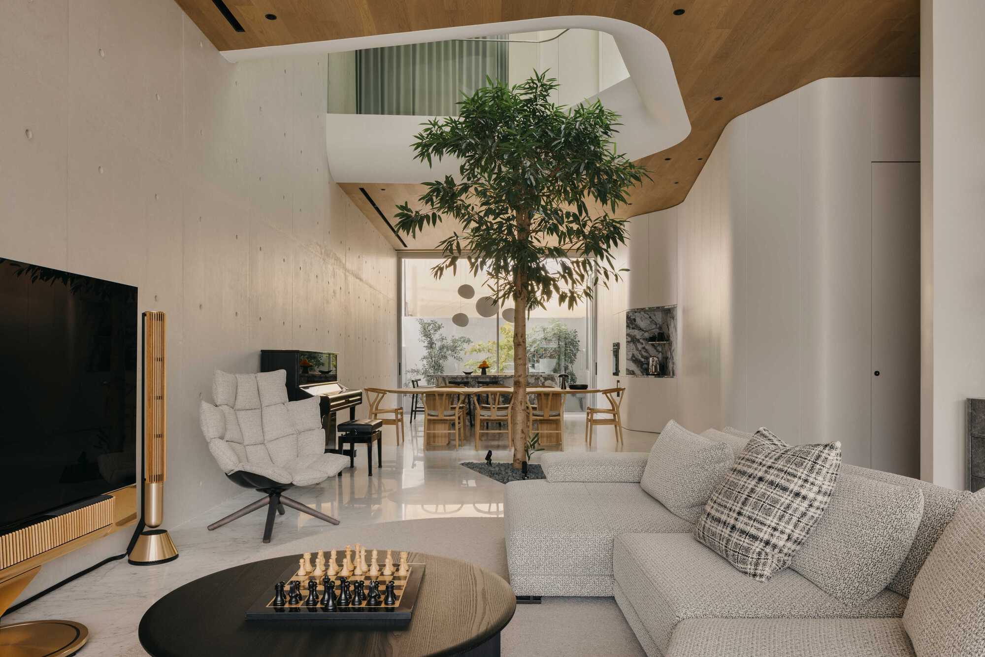 Double-height living space with central tree beneath a curved skylight and wooden ceiling