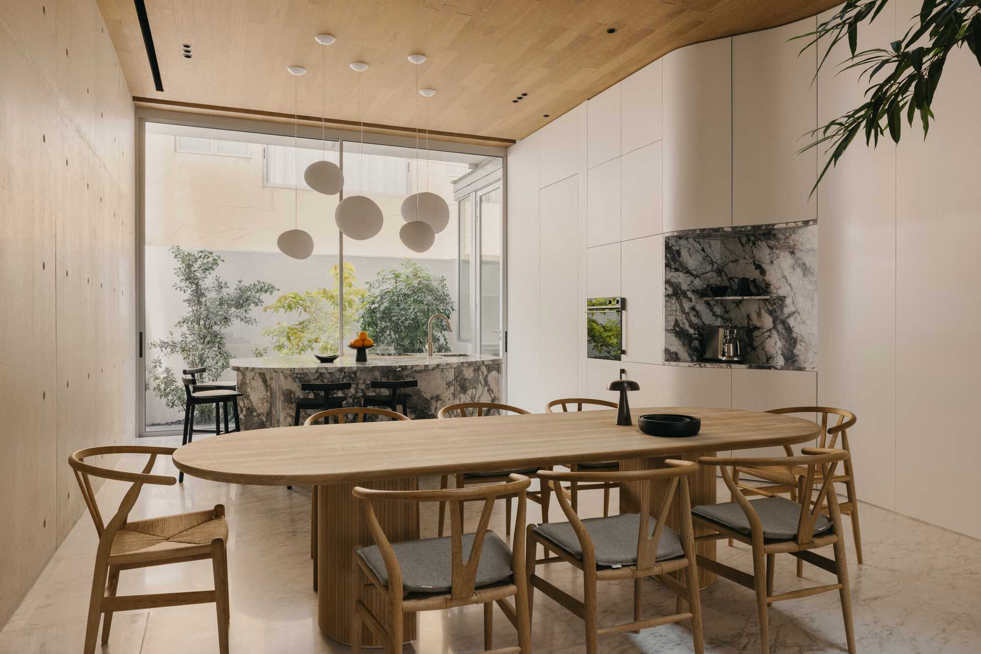 Dining area with oval timber table overlooking a planted courtyard through floor-to-ceiling glazing