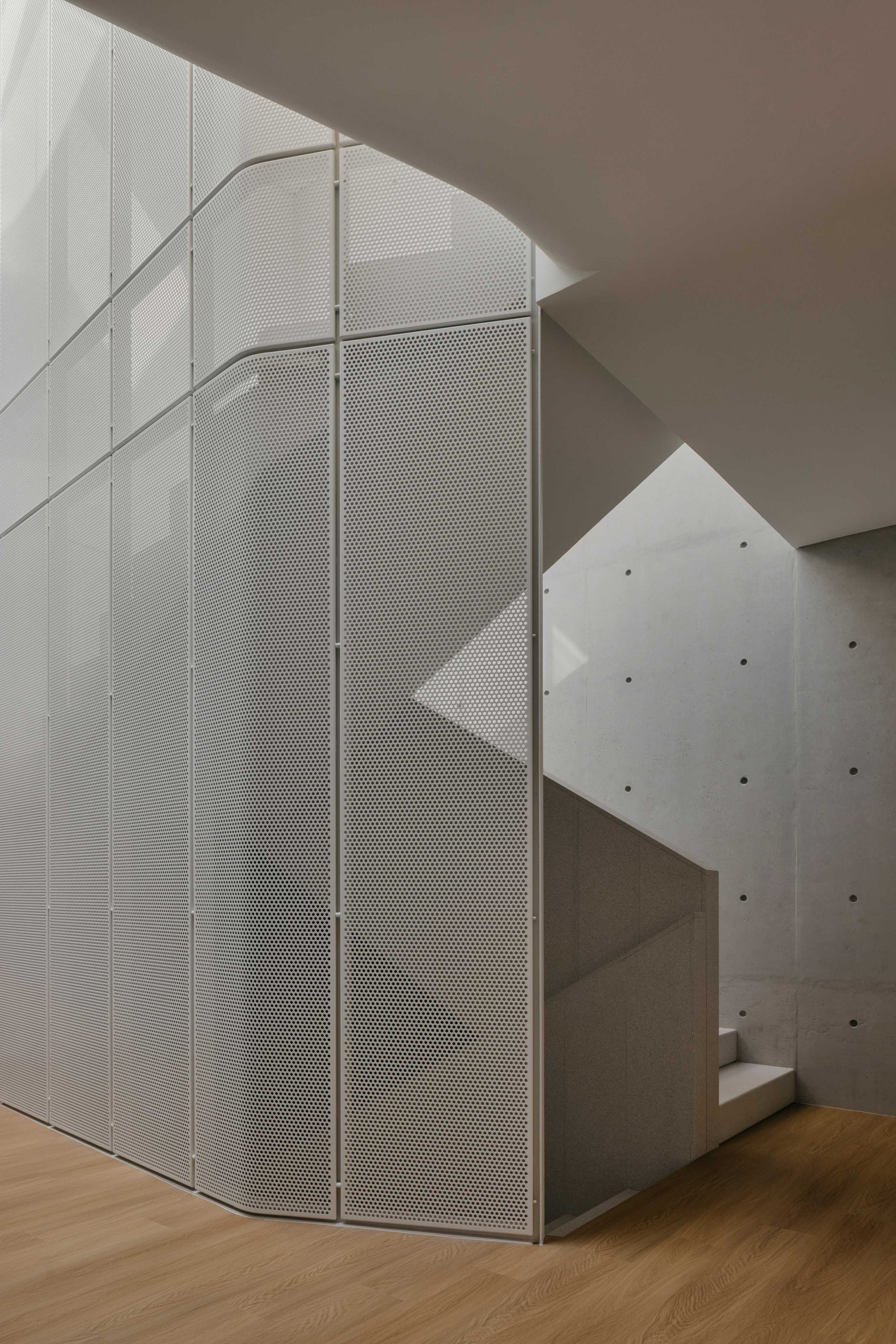 Curved perforated metal screen wrapping a corner beside a concrete staircase under natural light