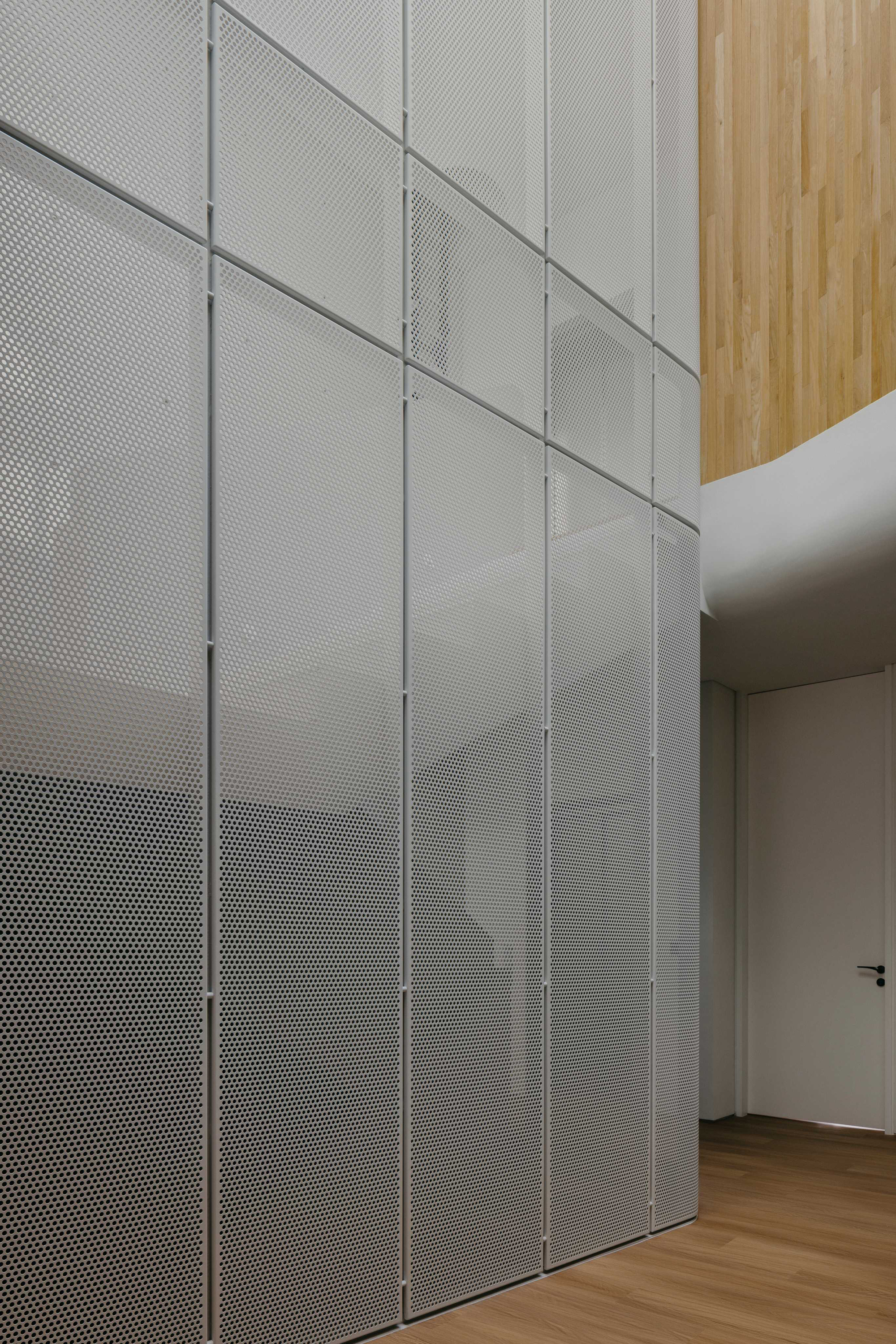 Perforated metal panel wall with diagonal handrail shadows and timber ceiling insert above