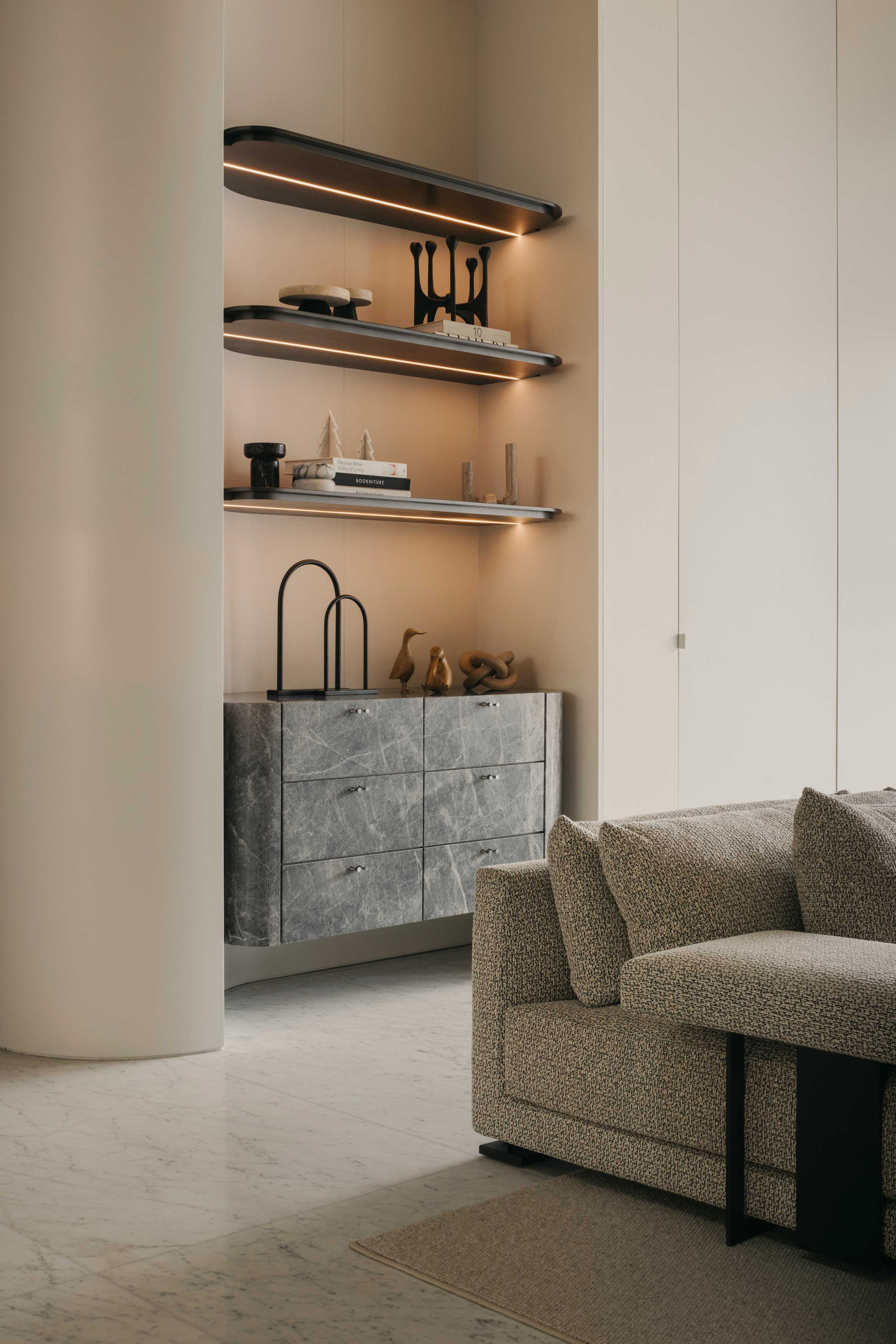 Living room niche with backlit floating shelves above a grey stone credenza and rounded column