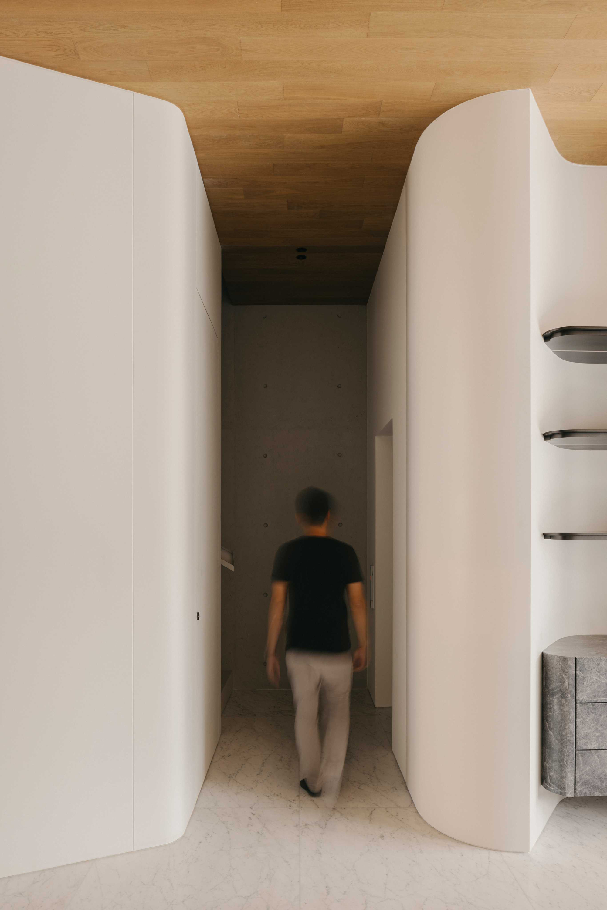 Narrow corridor with curved white walls and timber ceiling as a person walks toward the far room