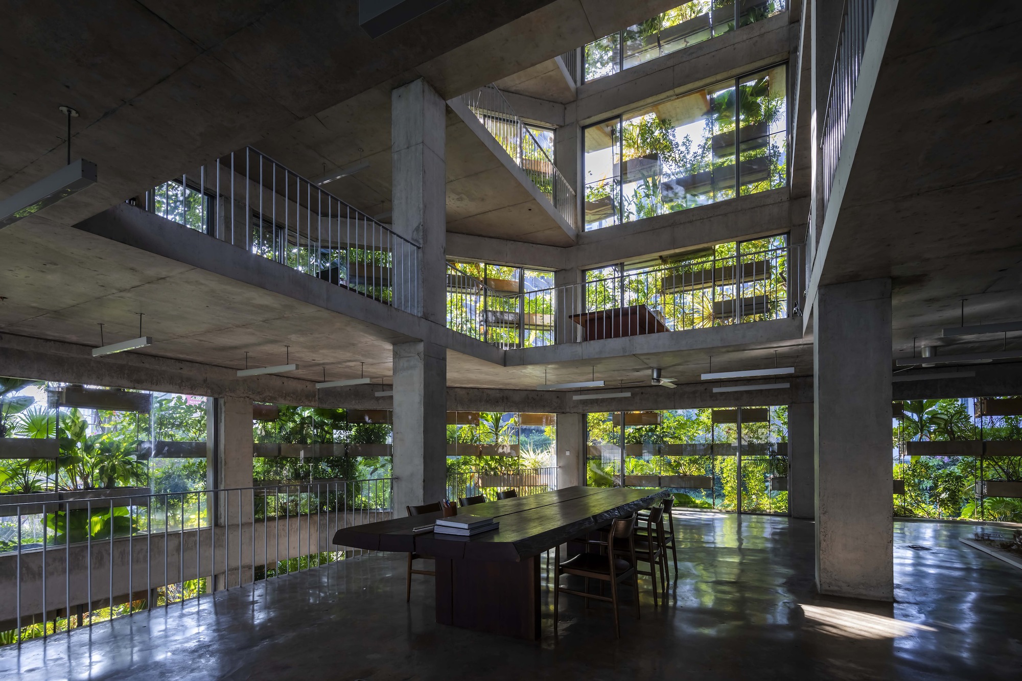 Interior atrium with concrete columns and cantilevered floors framing planted balconies in dappled sunlight