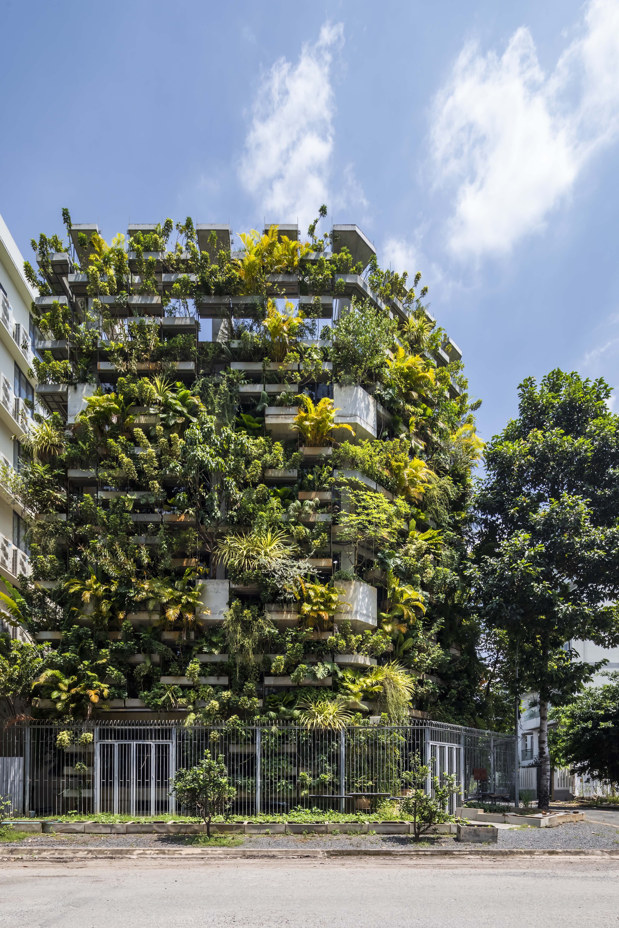 Street view of the planted balcony facade covered with dense tropical vegetation under blue sky
