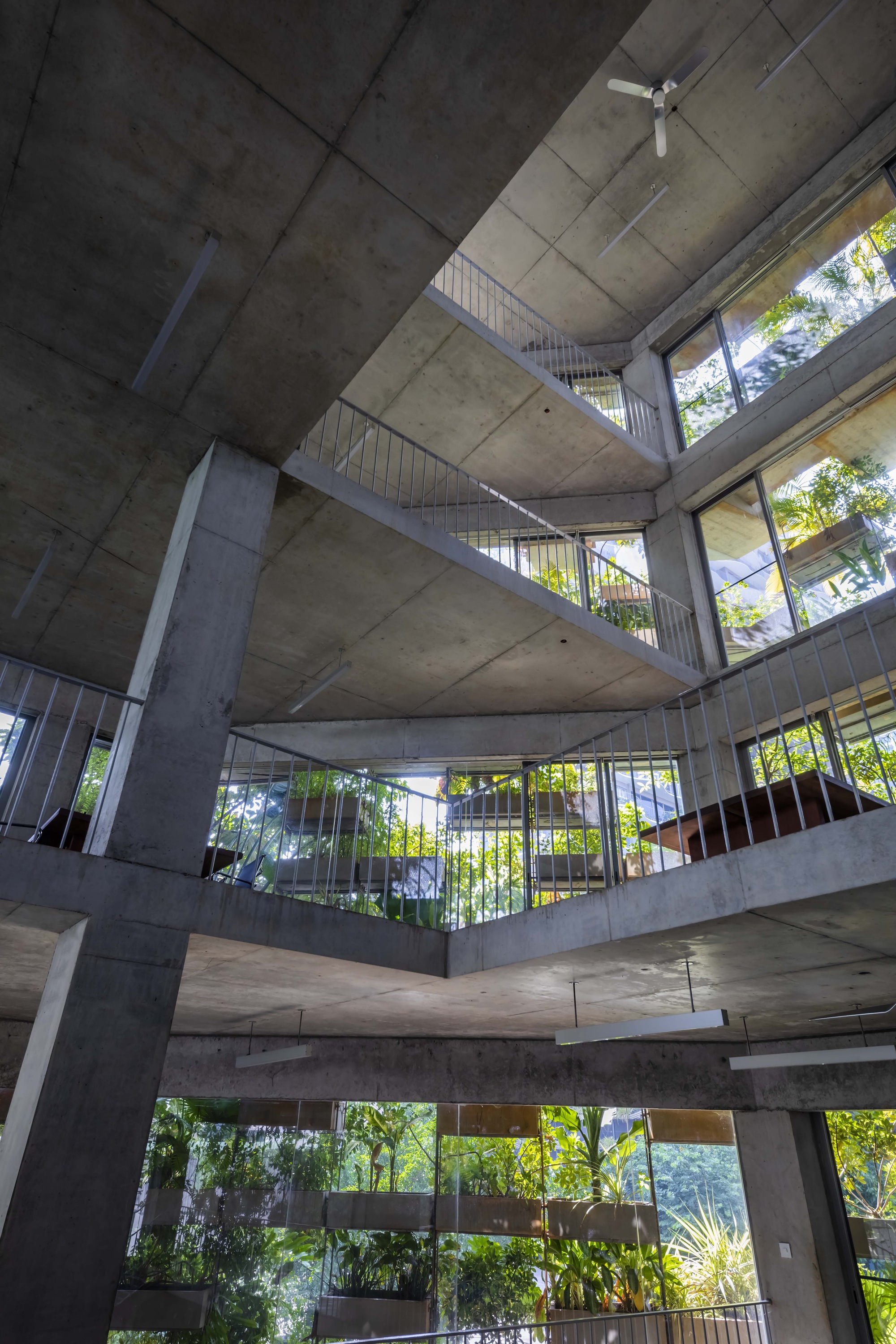 Upward view into the exposed concrete atrium with stacked balconies framing green trees beyond