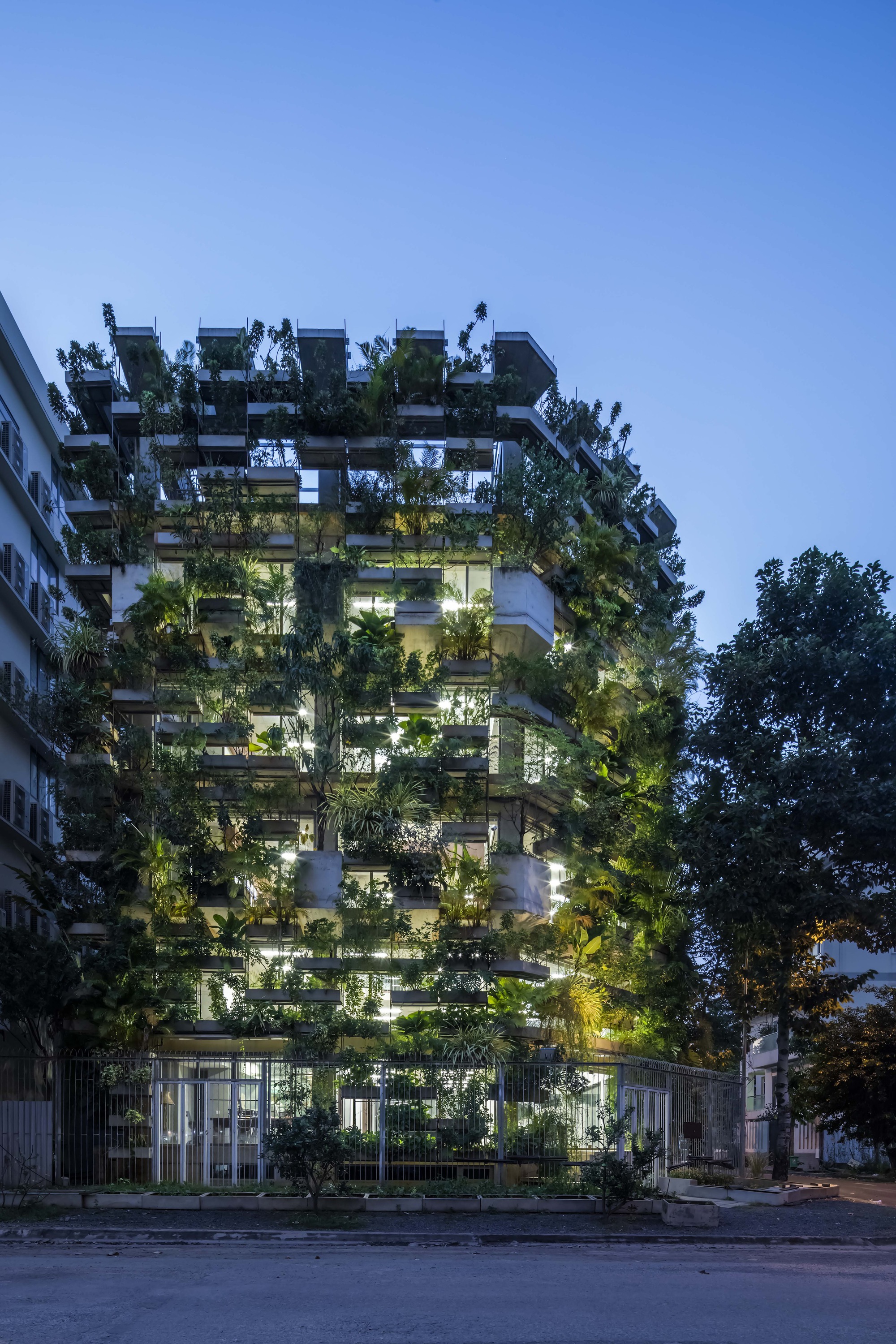 Street facade of the tower densely planted with trees on every balcony at twilight