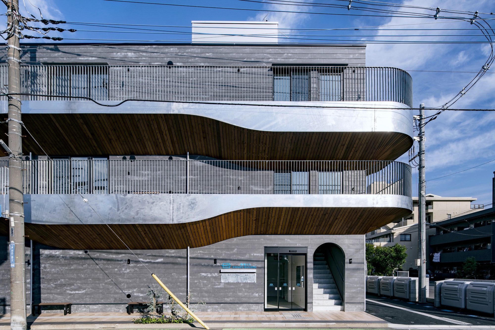 Front elevation showing the stacked cantilevered terraces with wood soffits and corrugated metal screening above stone base