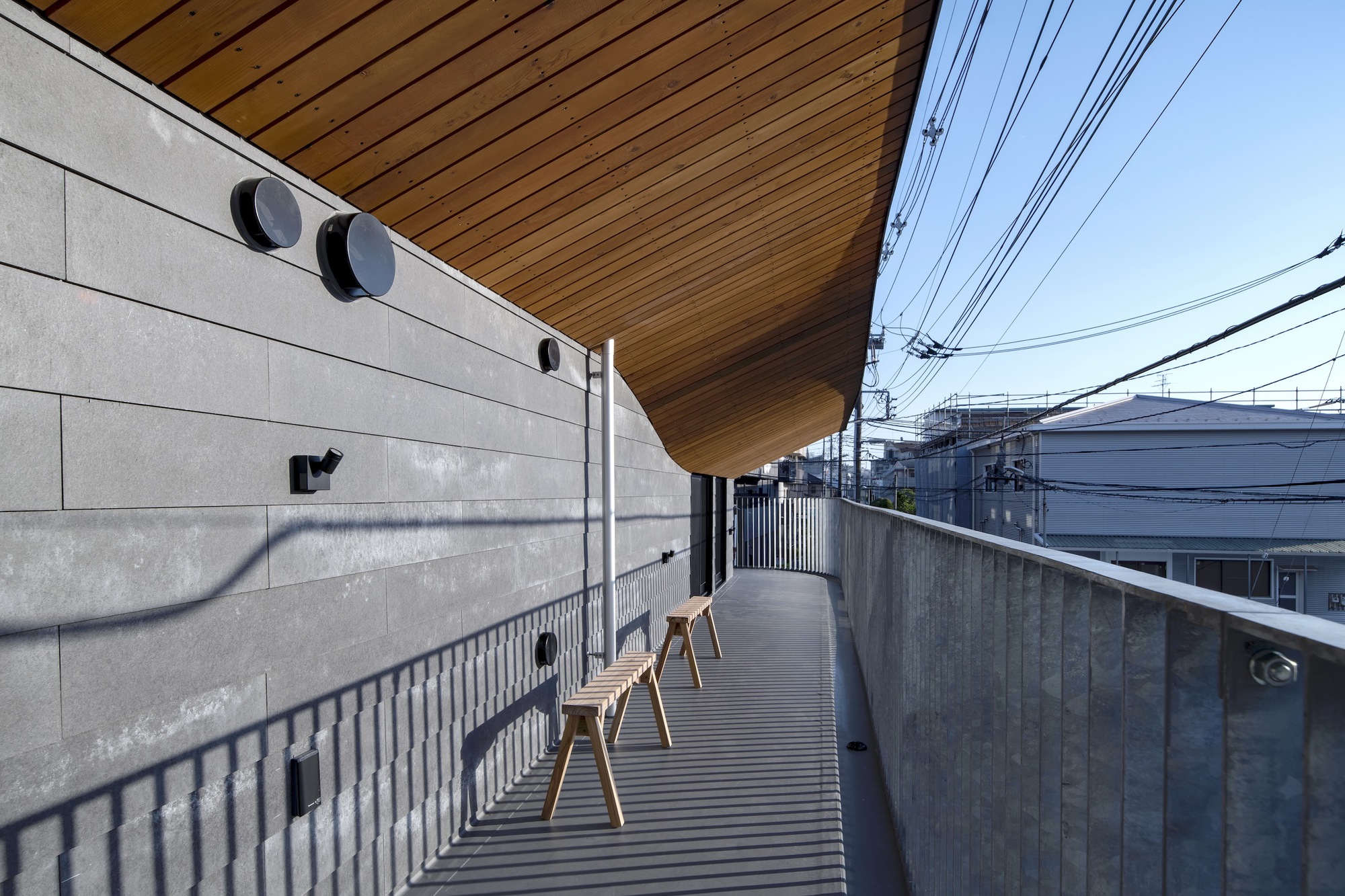 Upper level terrace with timber slat decking and wooden stools beneath the cantilevered wood ceiling