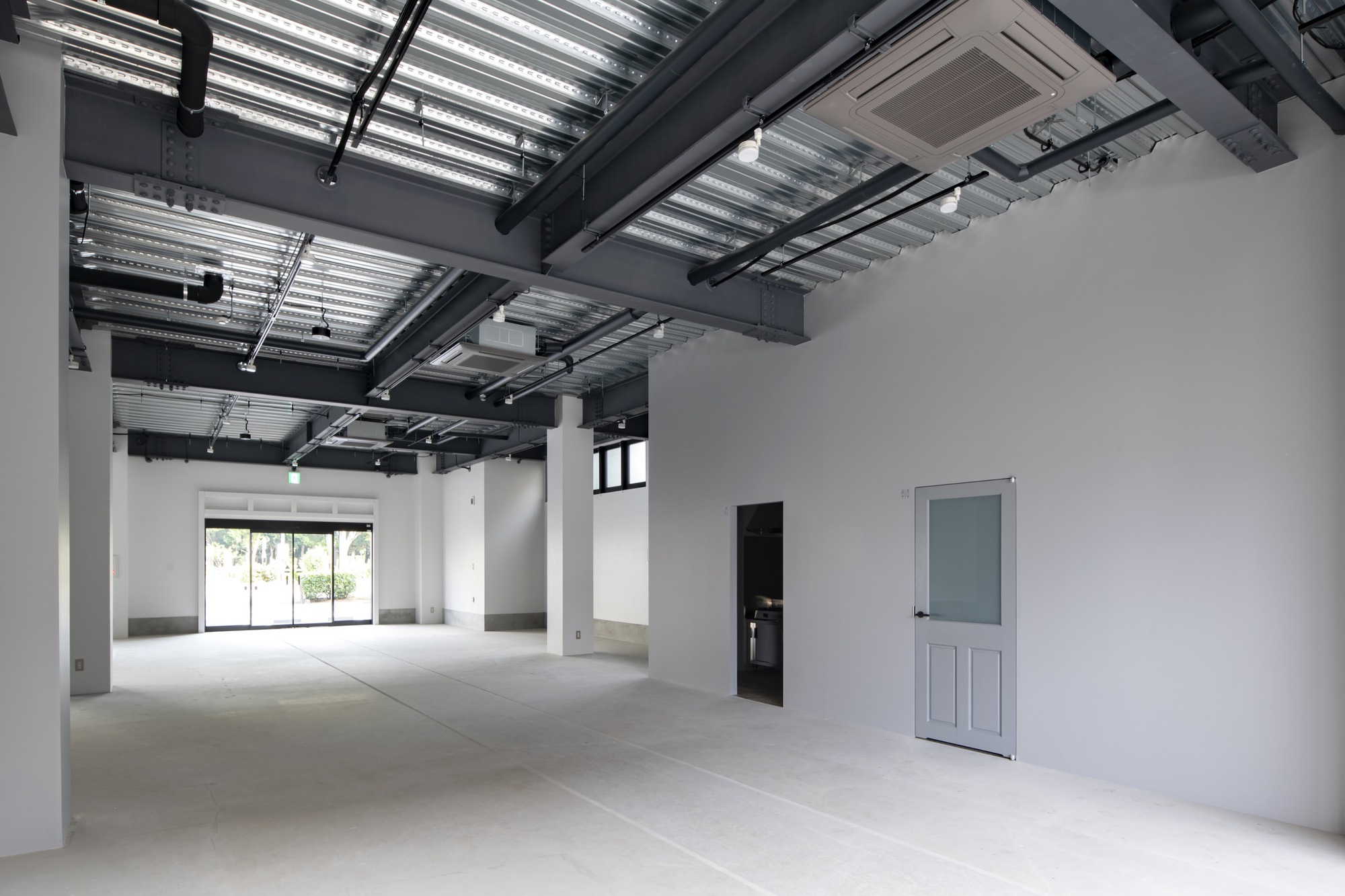 Interior space with exposed structural ceiling and white partition wall under ambient daylight