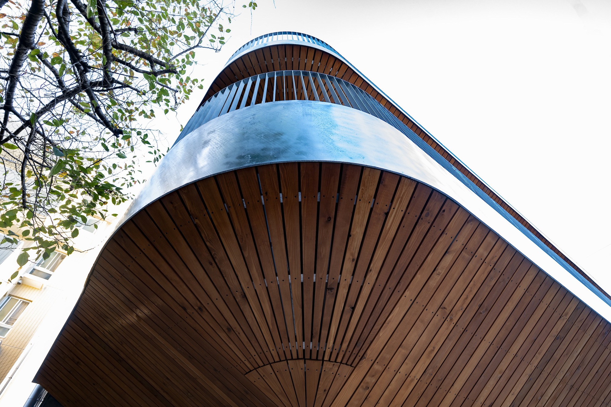 Upward view of the rounded balcony corner clad in vertical wood slats with metal edge trim