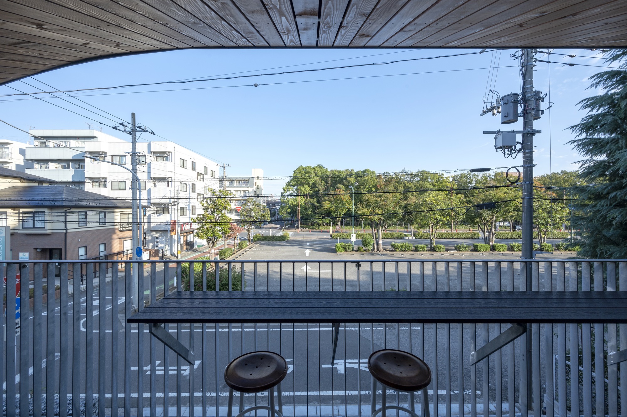 Upper level balcony with wood ceiling, metal railing and counter overlooking residential rooftops and trees