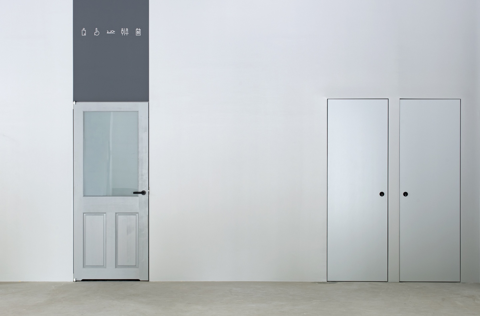 White wall with paneled door and pair of tall storage doors beside polished concrete floor