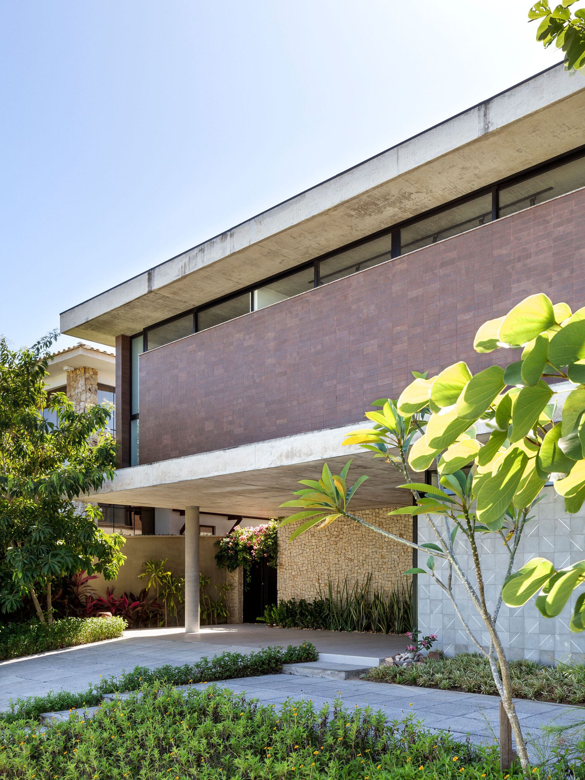 Cantilevered concrete slab shading the paved forecourt with planted beds and geometric textured wall below