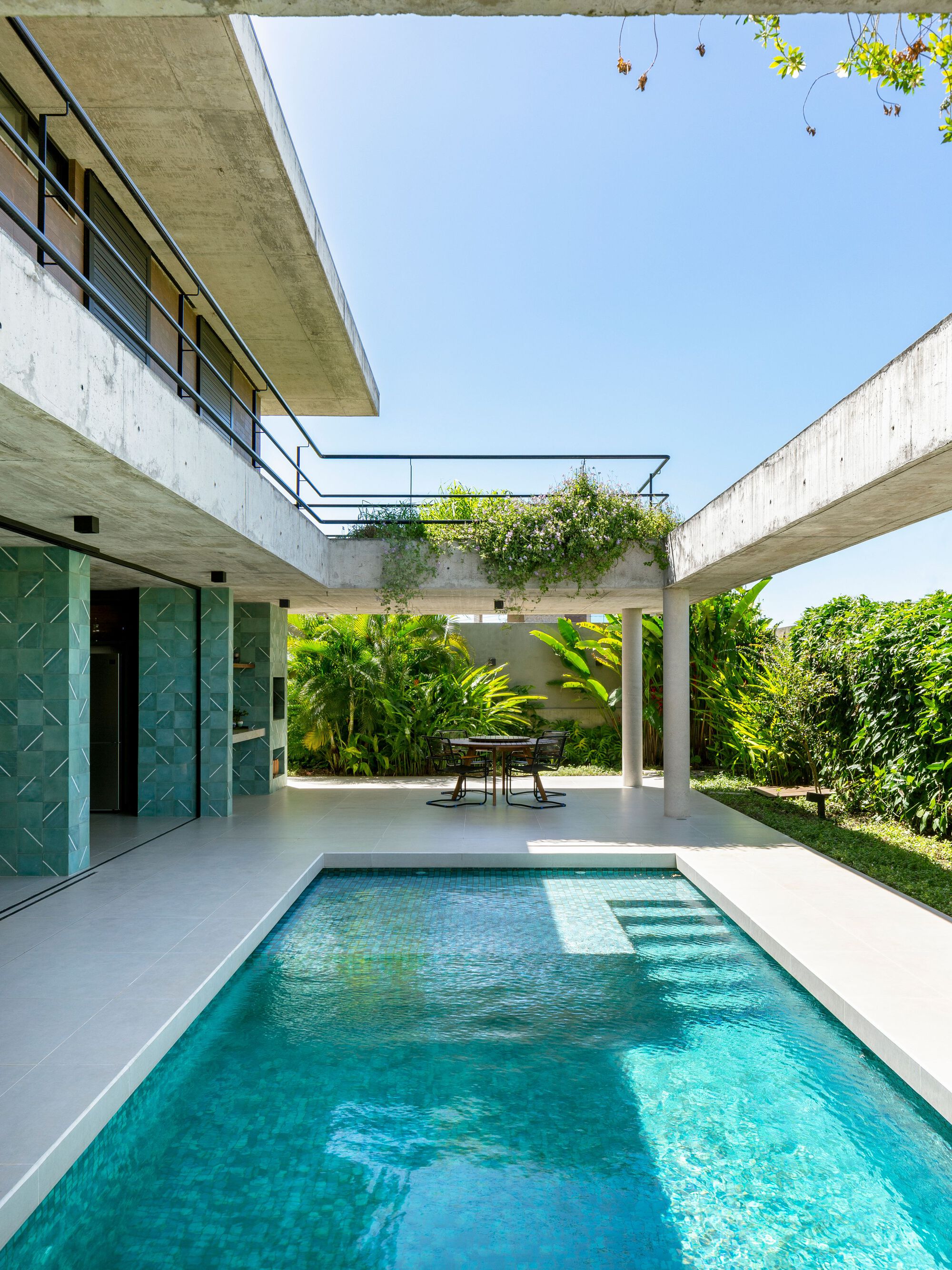 Pool terrace framed by concrete beams and planted green roof connecting two wings of the residence