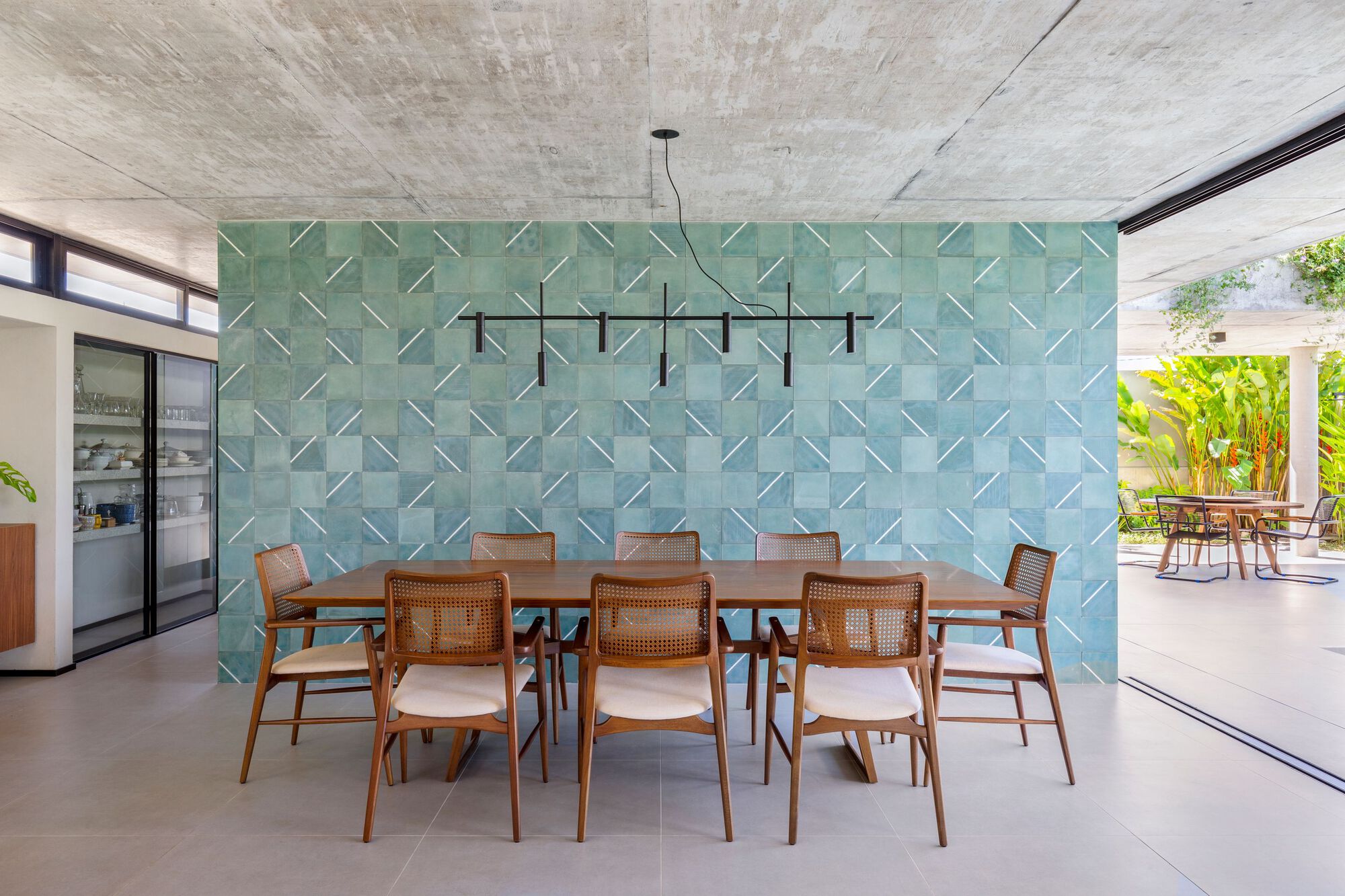 Dining area with turquoise relief tile wall and exposed concrete ceiling opening to the pool terrace