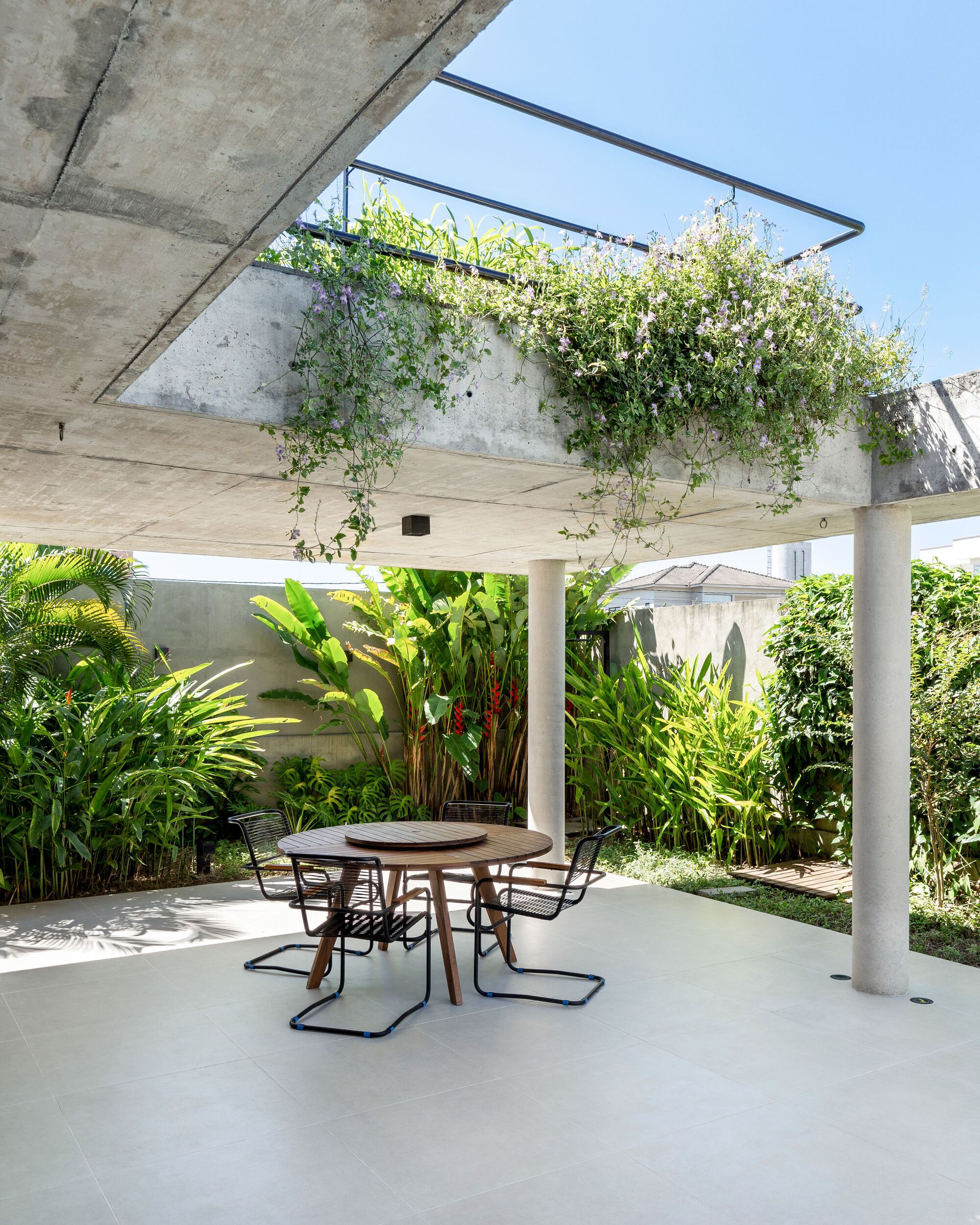 Covered terrace with exposed concrete soffit, hanging planter above and tropical vegetation around dining furniture