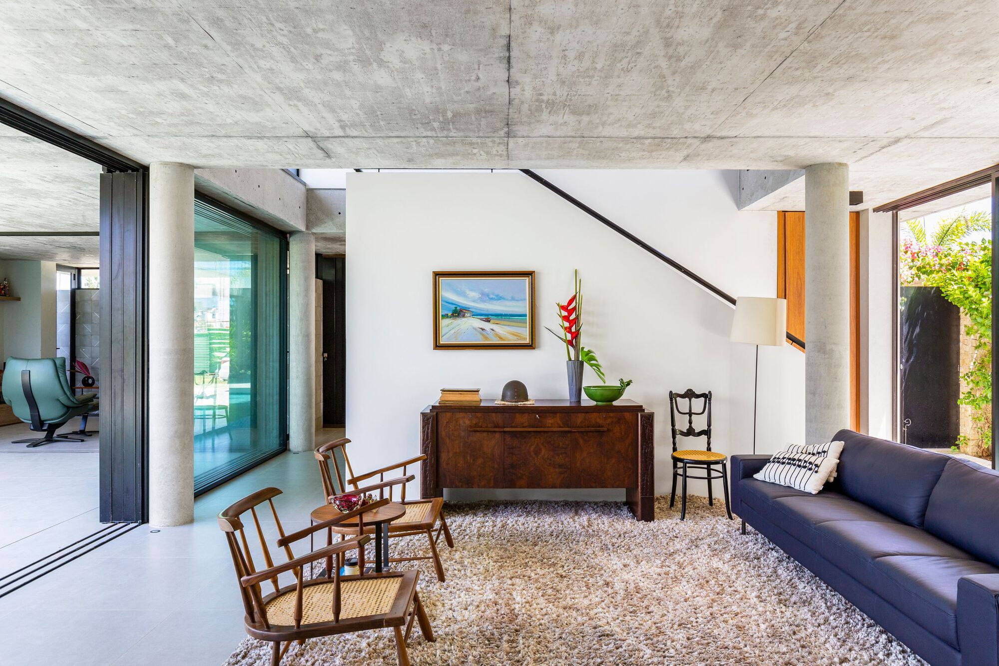 Double-height living area with board-formed concrete ceiling and circular concrete column beside wooden credenza