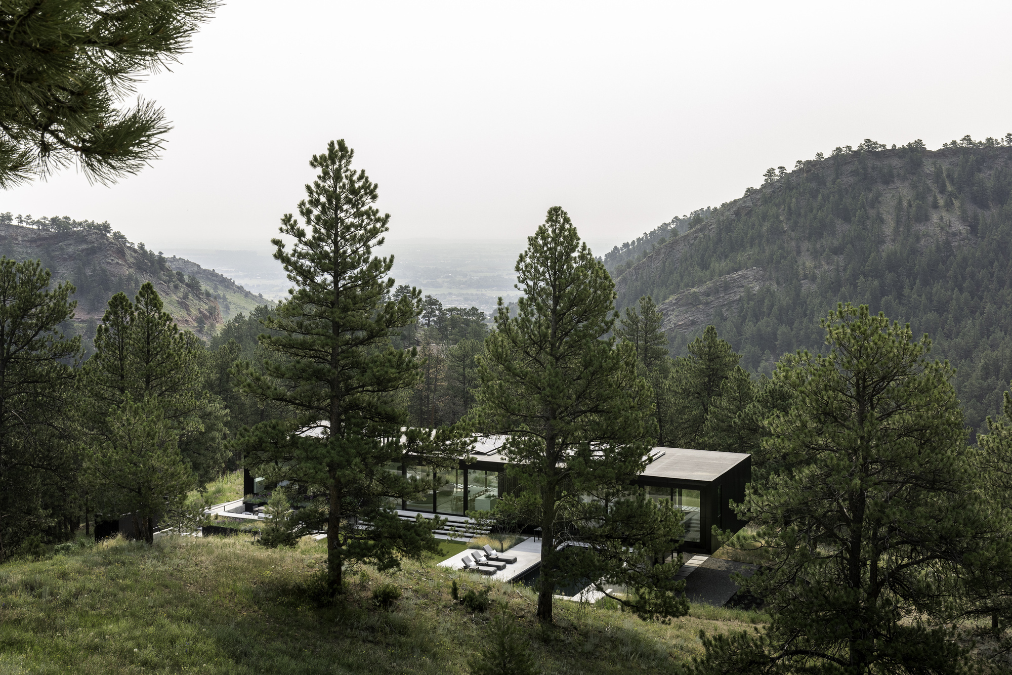 Hillside view of the residence nestled among pine trees with mountain ridges visible in the distance