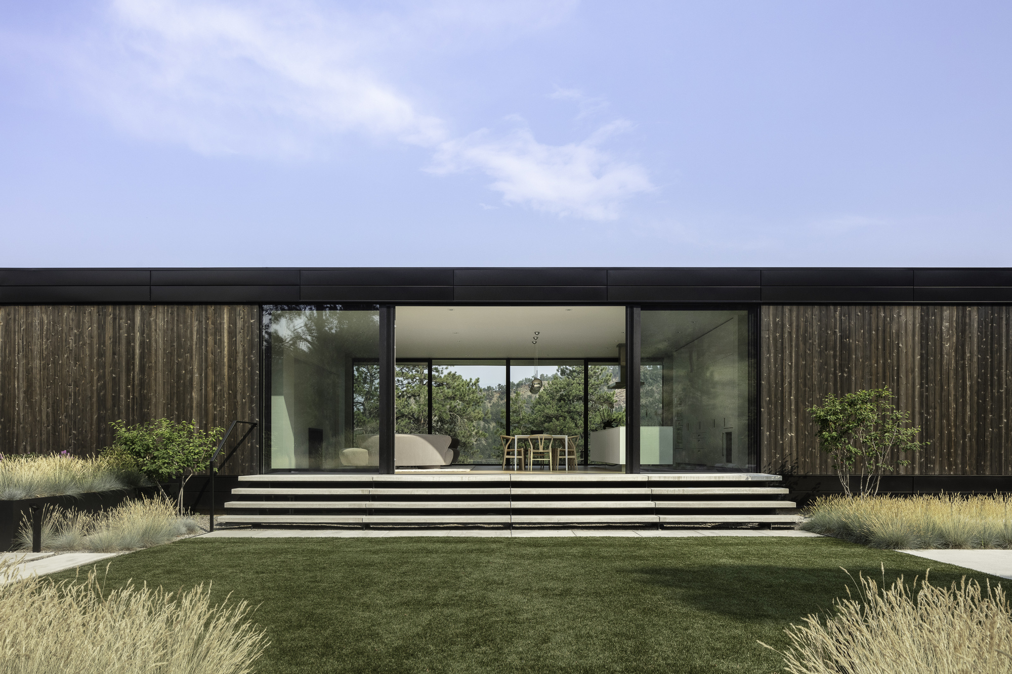 Wide concrete steps lead to the glazed facade with vertical timber cladding under an overcast sky