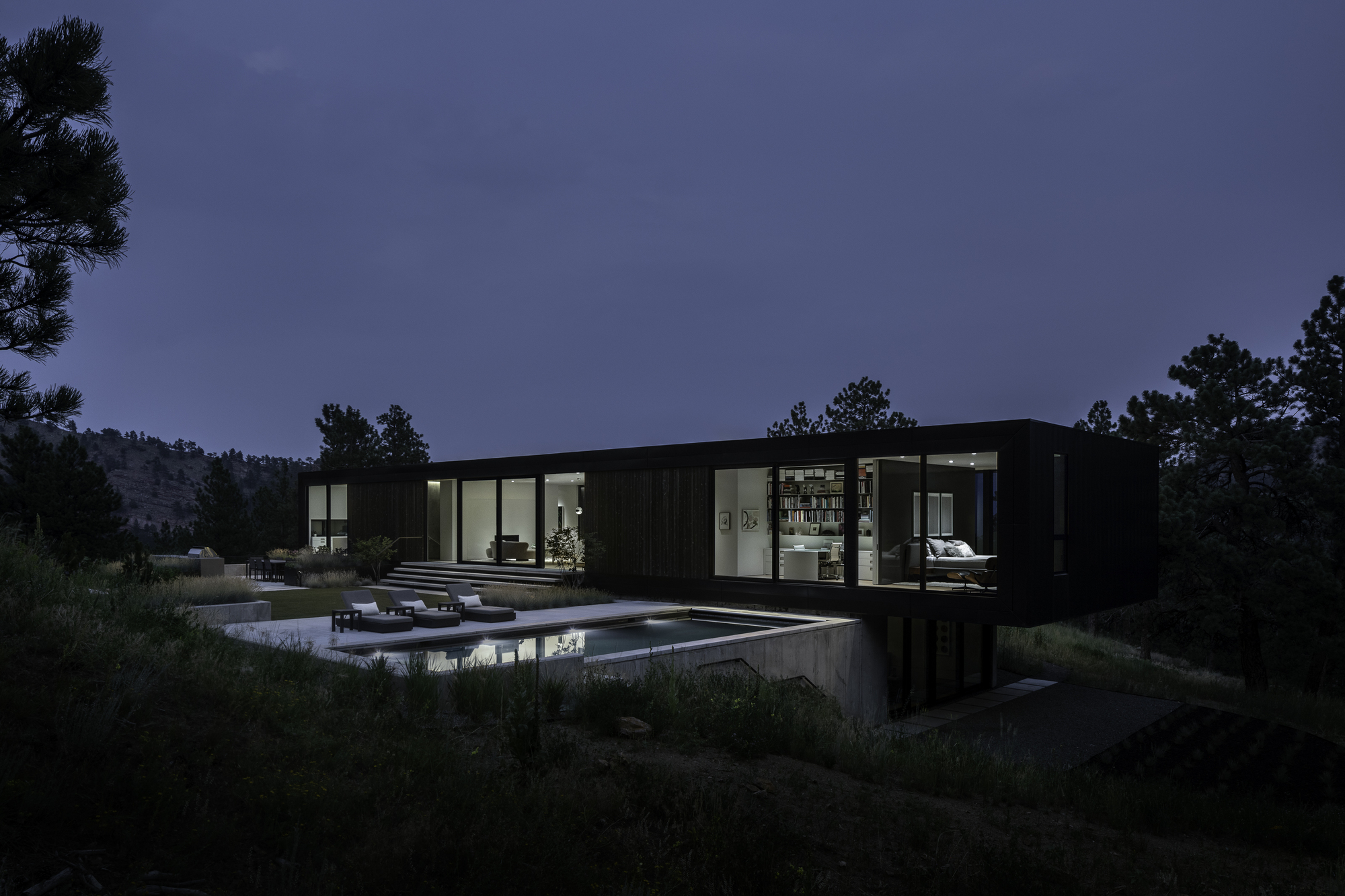 Black cladded residence with glazed openings above a concrete plinth and reflecting pool at twilight