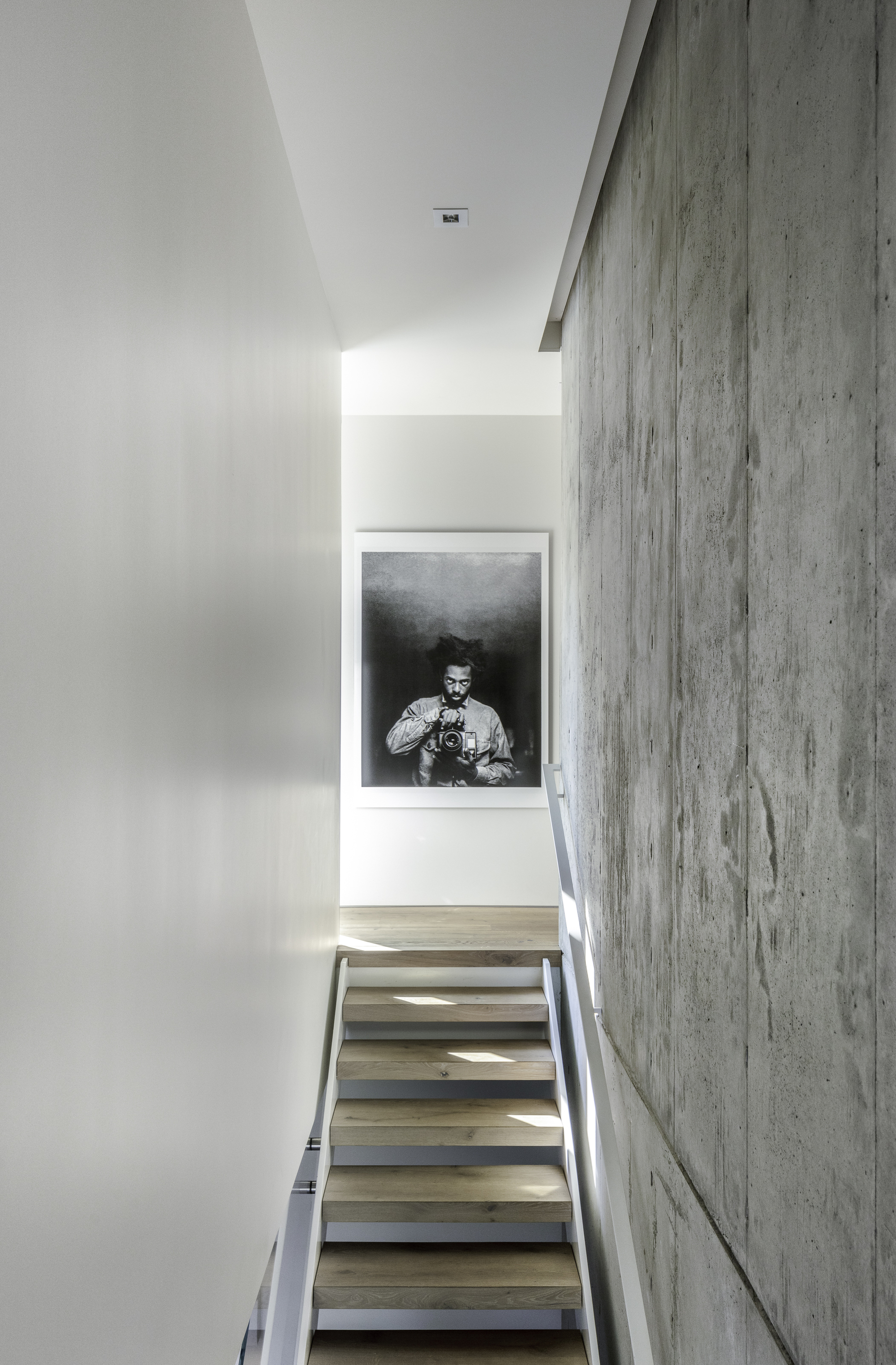 Staircase with floating timber treads alongside a board-formed concrete wall and framed photograph