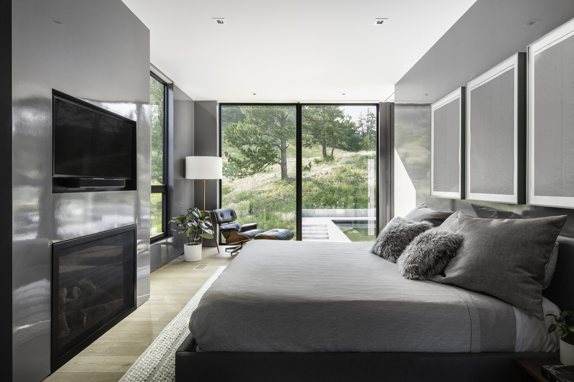 Bedroom with floor-to-ceiling glass doors opening to a grassy slope under afternoon light