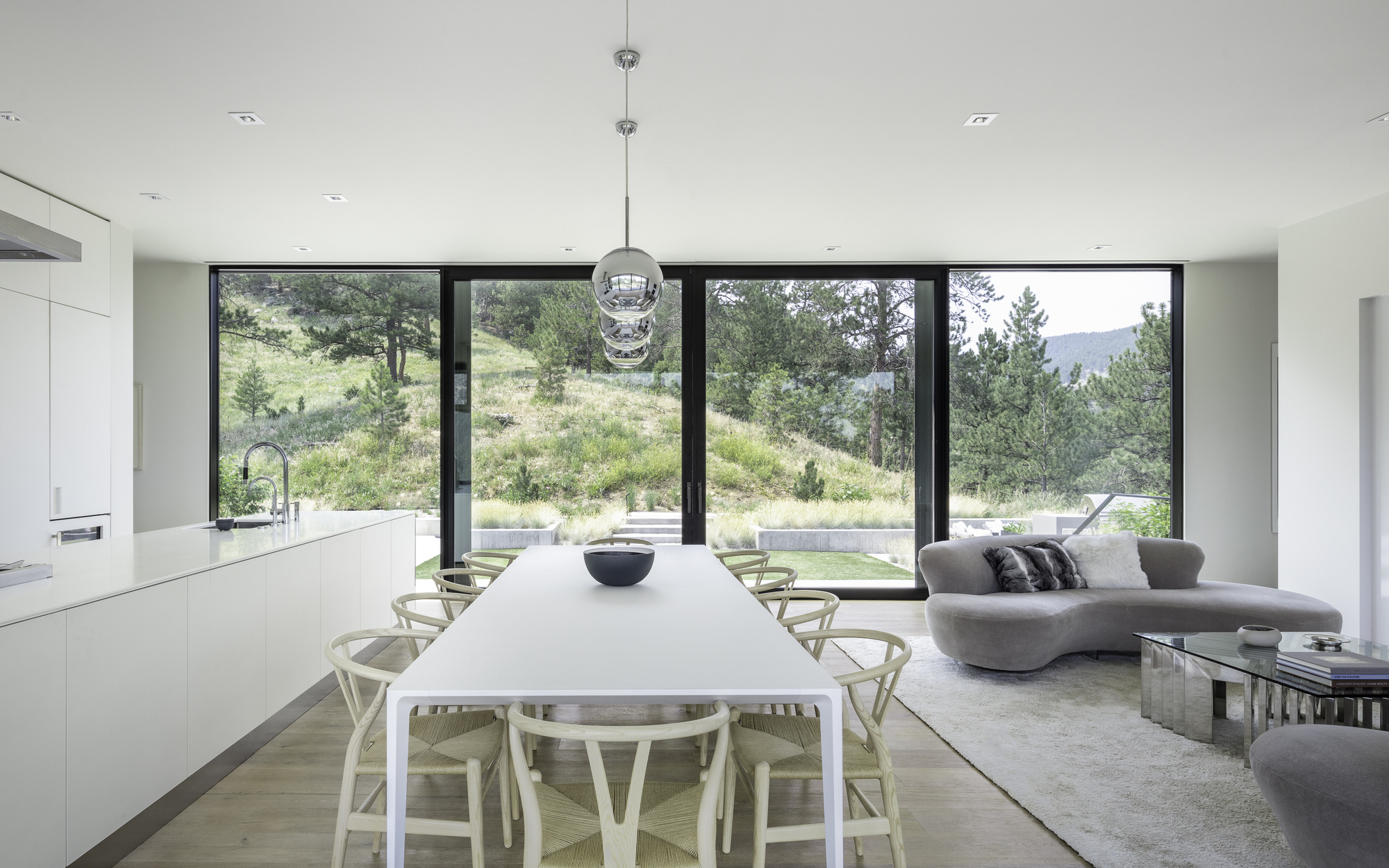 Open plan living and dining space with full-height glazing framing views of the hillside landscape