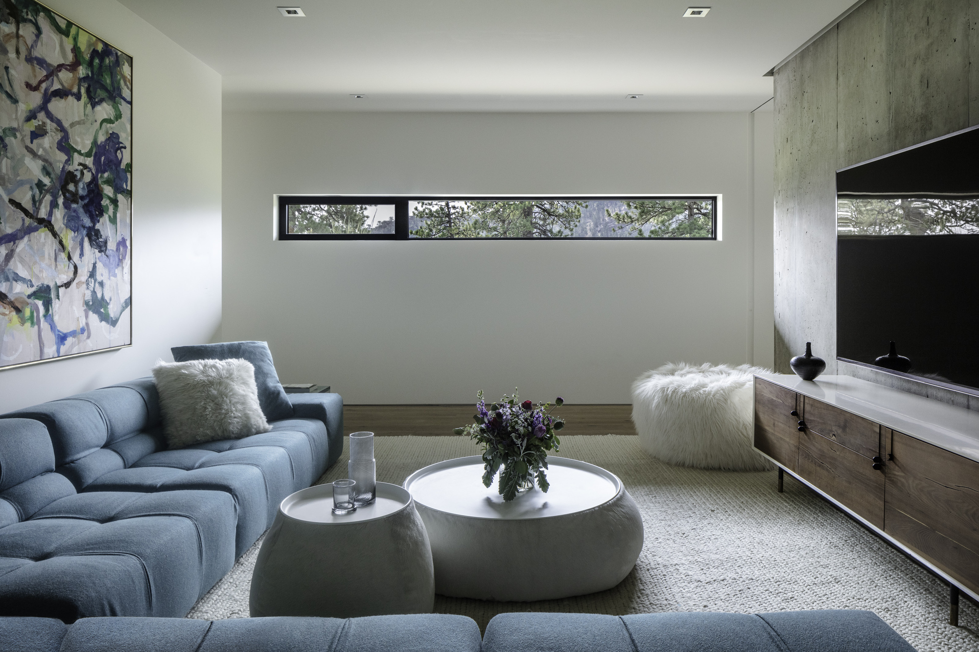 Living room with board-formed concrete accent wall and horizontal ribbon window framing foliage
