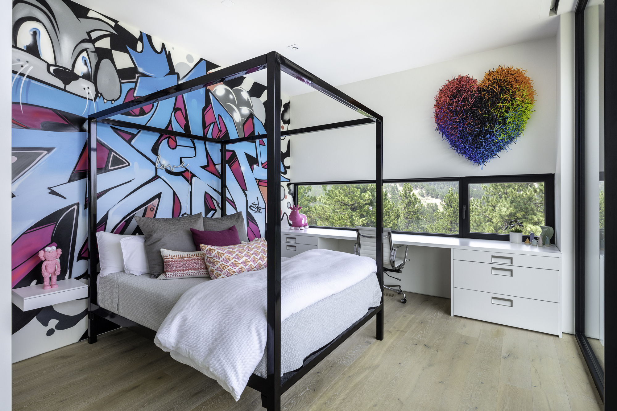 Bedroom with black canopy bed against a graffiti mural wall and ribbon window with shade