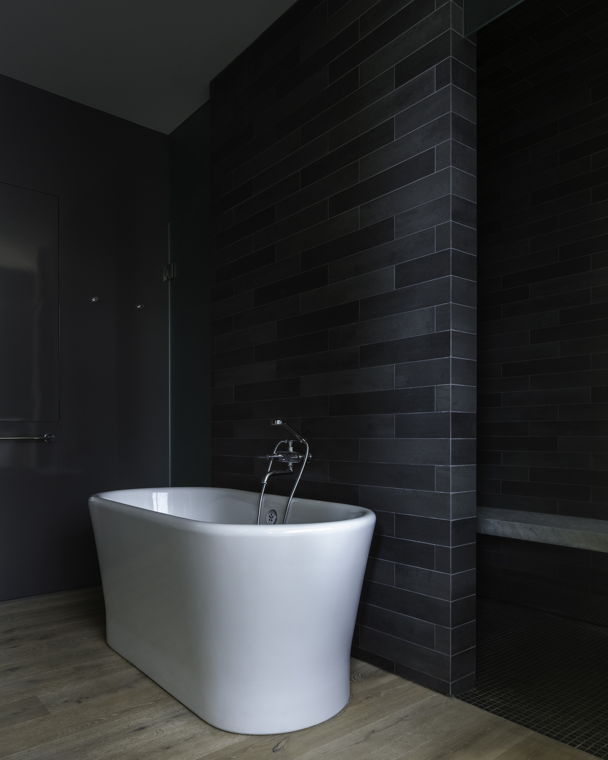 White freestanding bathtub against a dark brick tile wall in a dimly lit bathroom