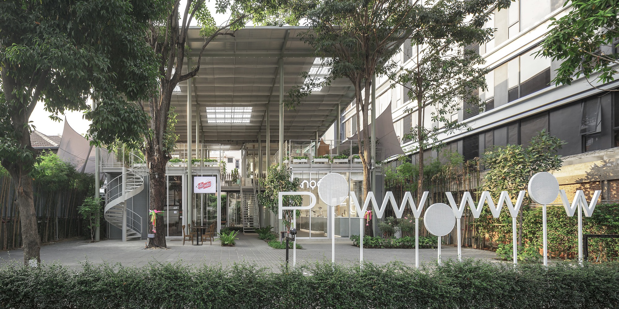 Courtyard view of the elevated pavilion with exposed steel structure and translucent roof panels framed by trees
