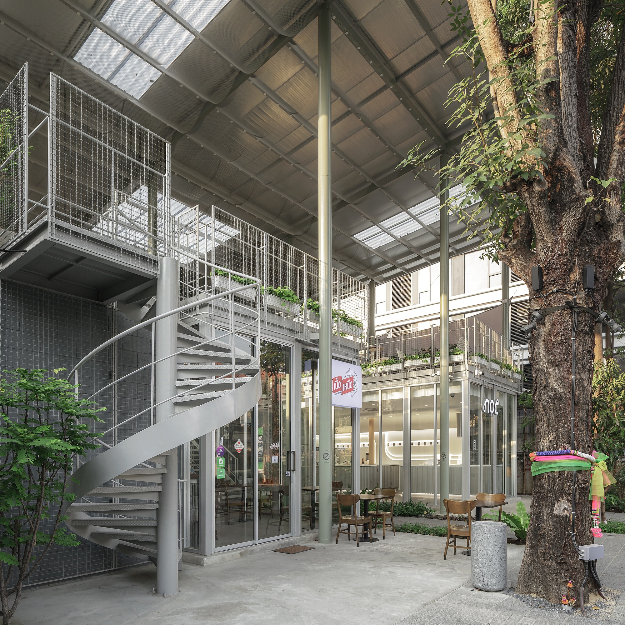 Interior courtyard with a helical steel staircase, glazed volumes and a preserved tree with exposed roots