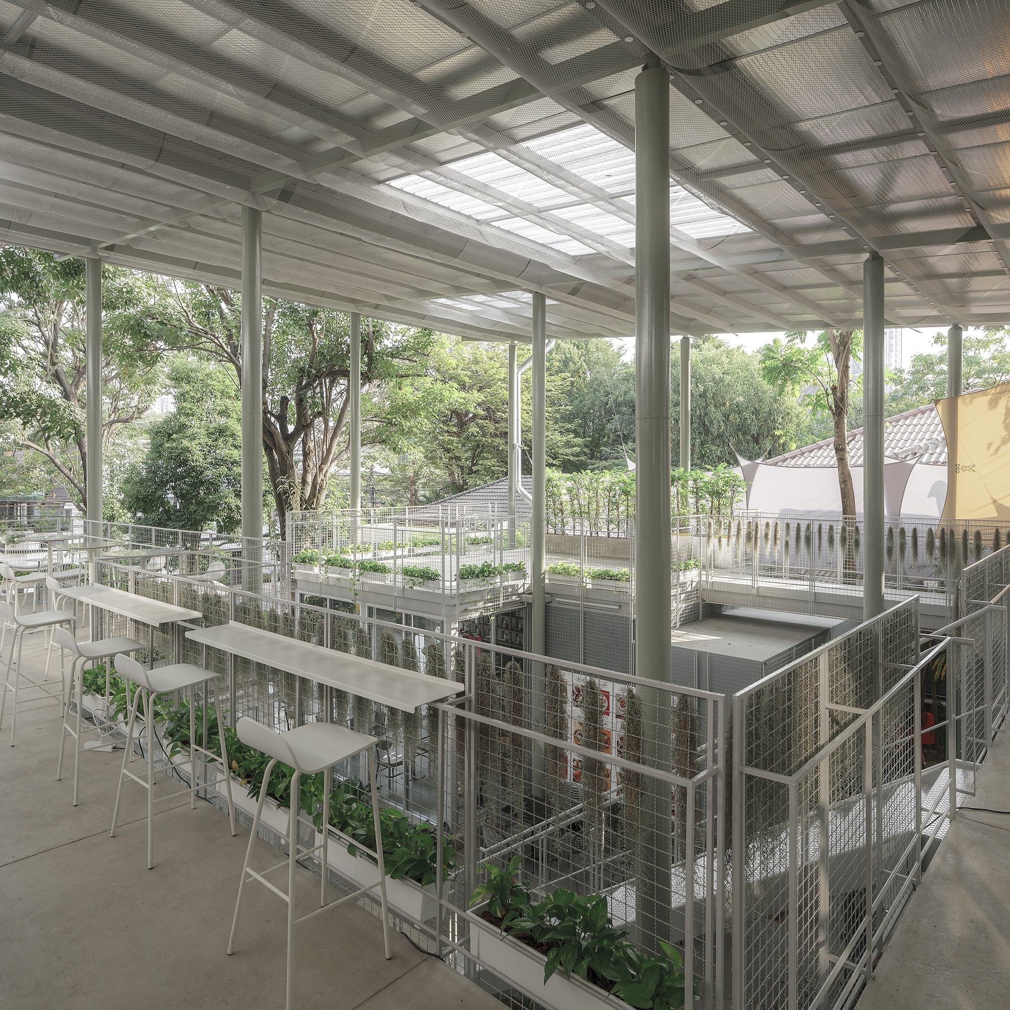 Upper level terrace with wire mesh railings, white bar seating and skylights in the corrugated metal roof