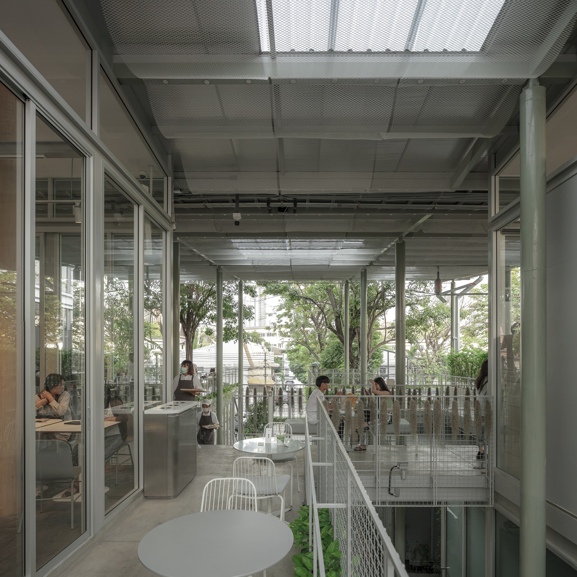 Corridor along glazed walls overlooking a planted terrace with wire mesh railings and mature trees beyond