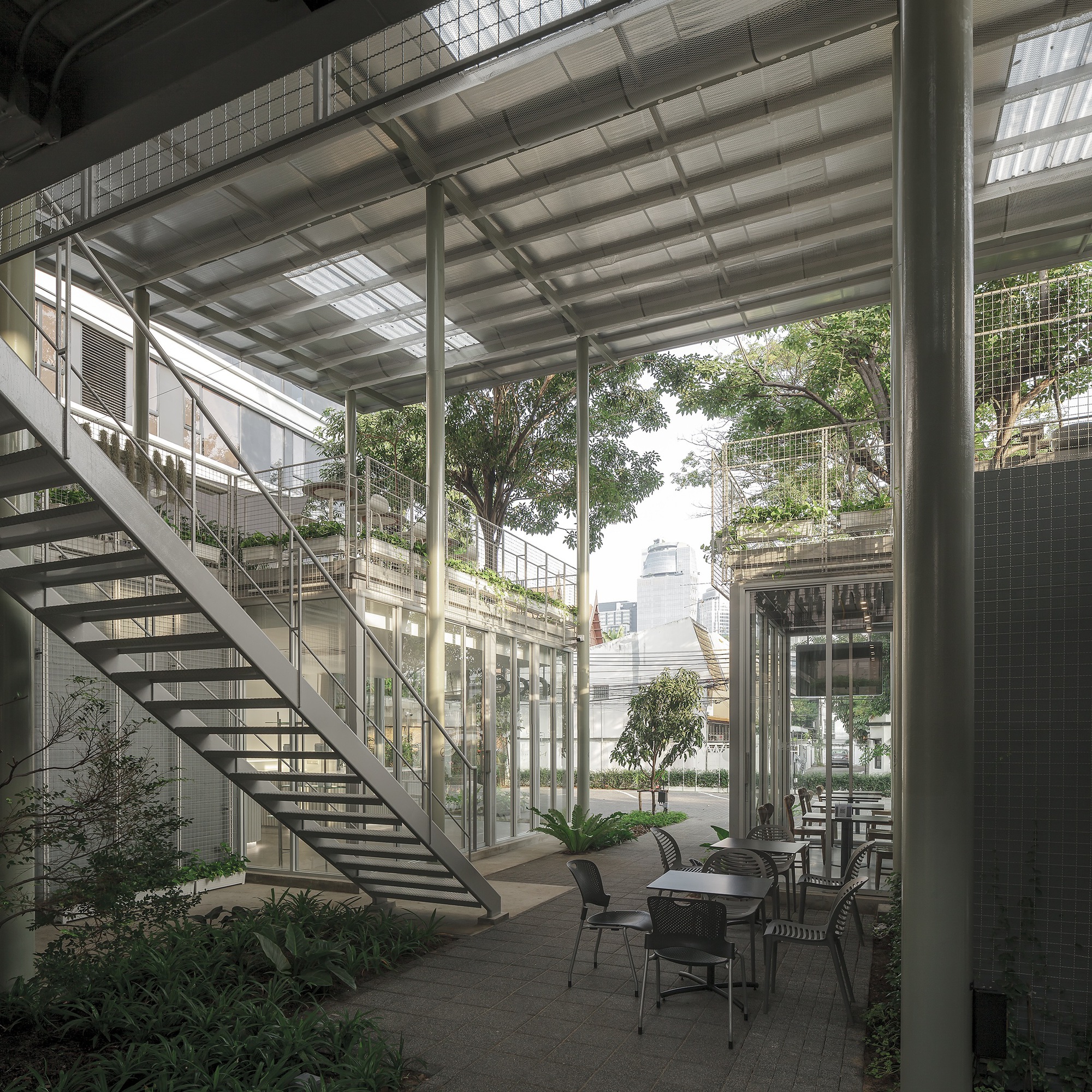 View across the courtyard showing the open-tread staircase, steel columns and planted ground-level terrace