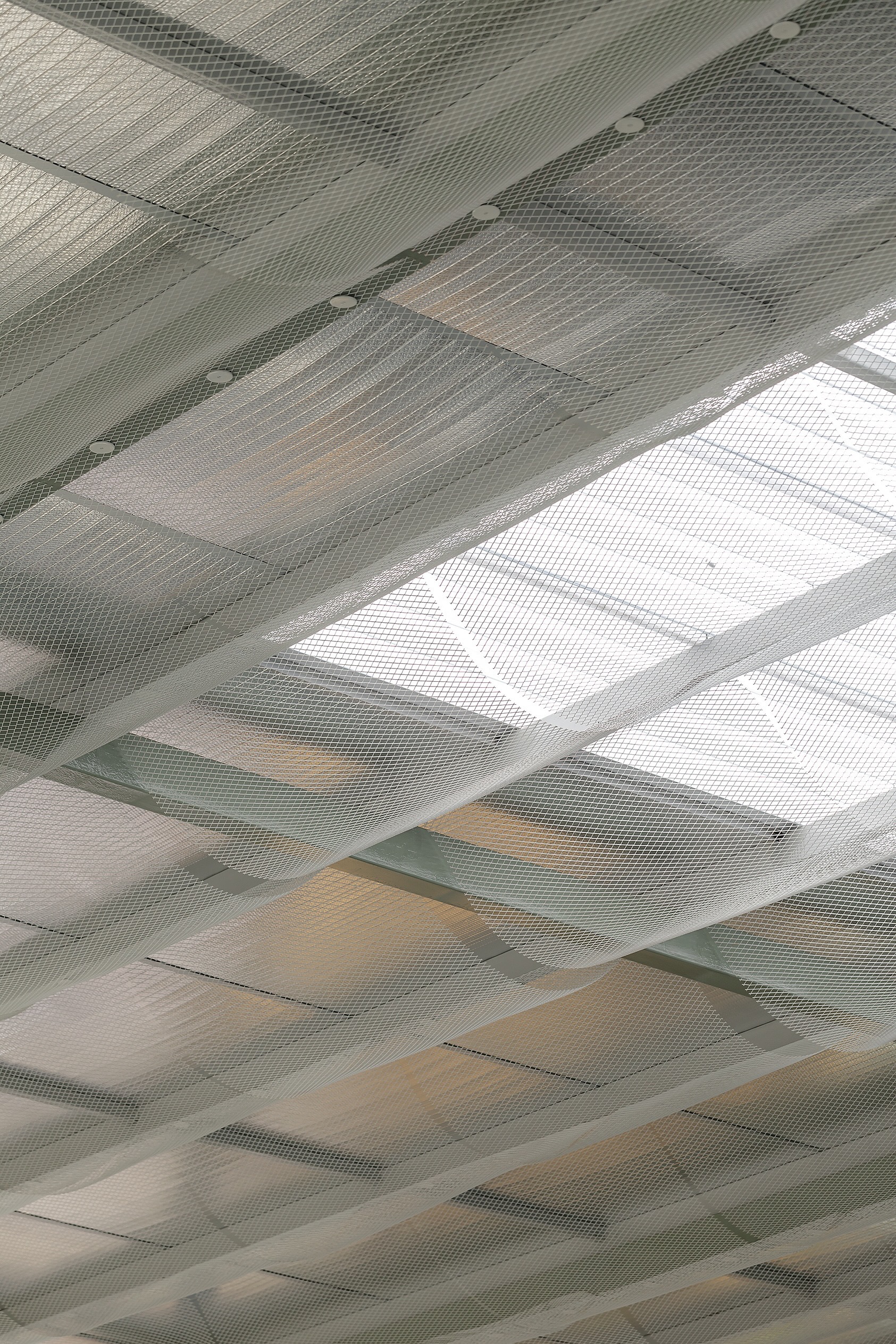 Perforated metal ceiling panels with integrated skylights casting geometric shadows across the surface