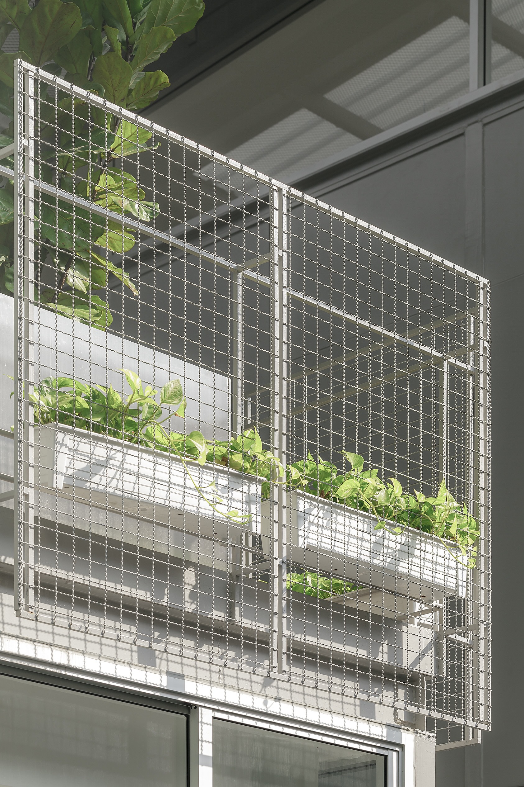 Wire mesh facade screen with integrated planter boxes holding foliage in bright daylight