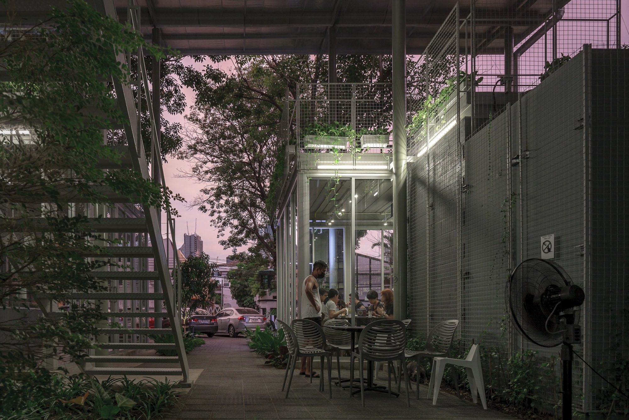 Covered ground-floor terrace with dining furniture surrounded by planted trees at twilight