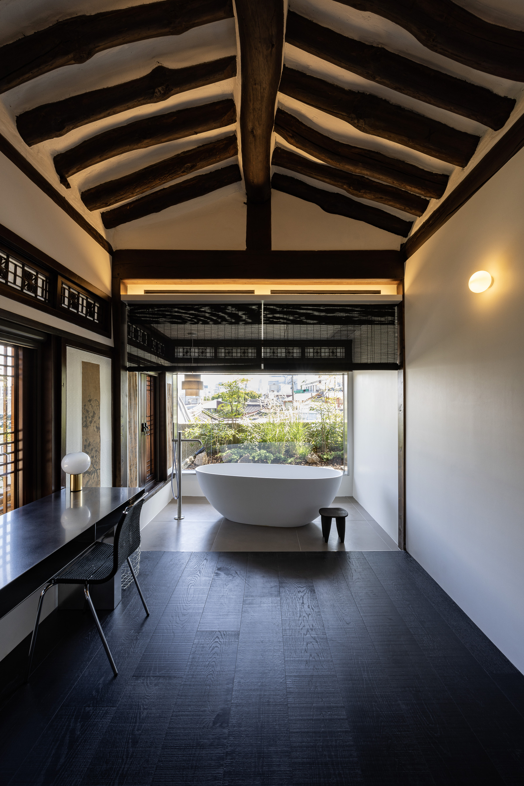 Freestanding bathtub beneath exposed timber rafters with a view to the planted courtyard