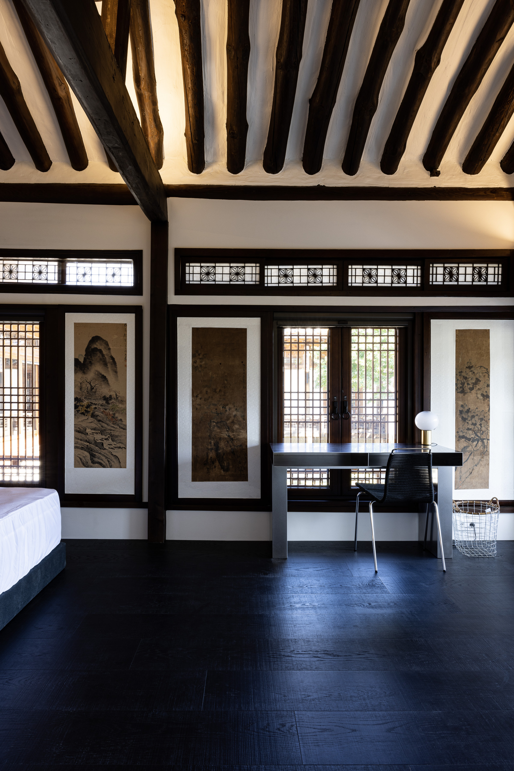 Room with exposed timber ceiling beams, latticed screens, framed scroll paintings, and dark wooden flooring