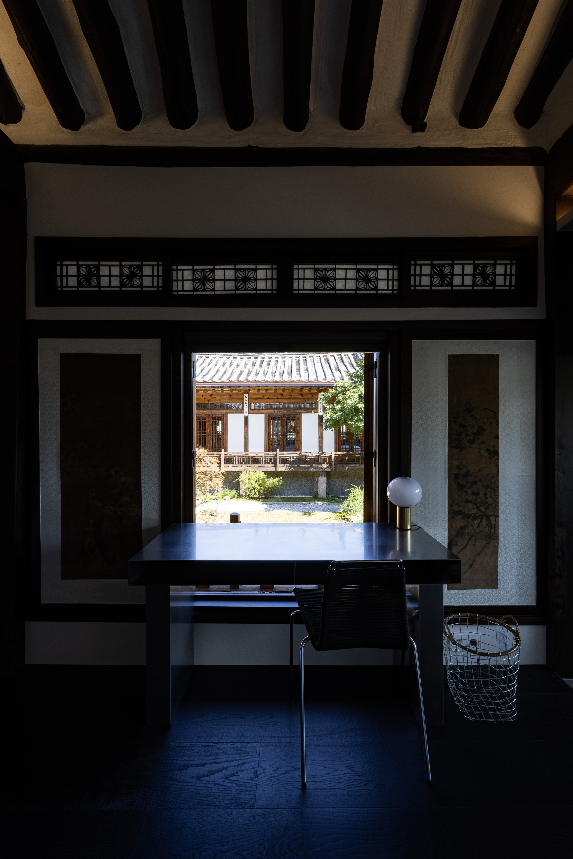 View through a dark timber-framed opening toward a courtyard with a tiled roof structure beyond