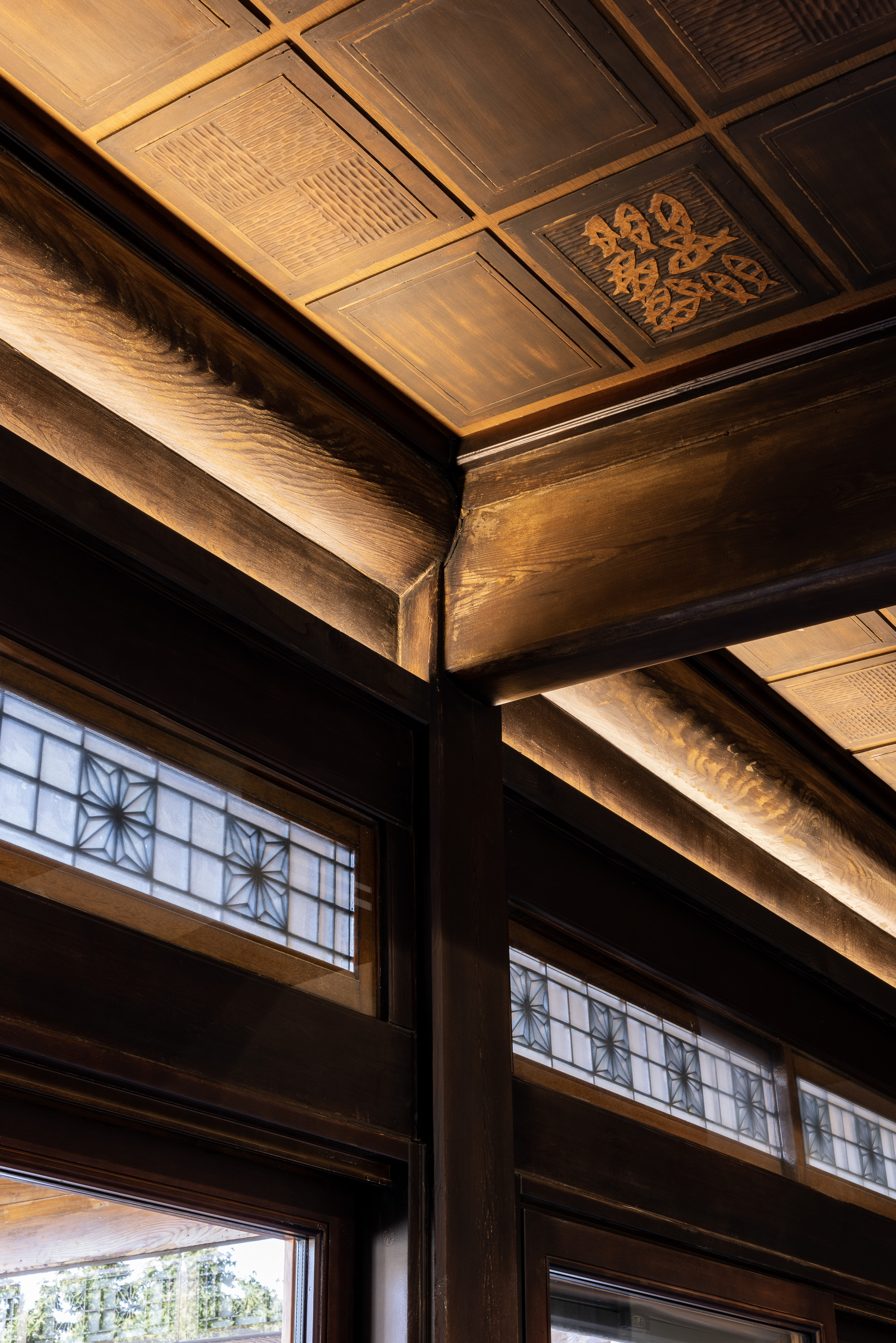 Upward view of timber ceiling beams with ornamental panels and lattice transom windows below