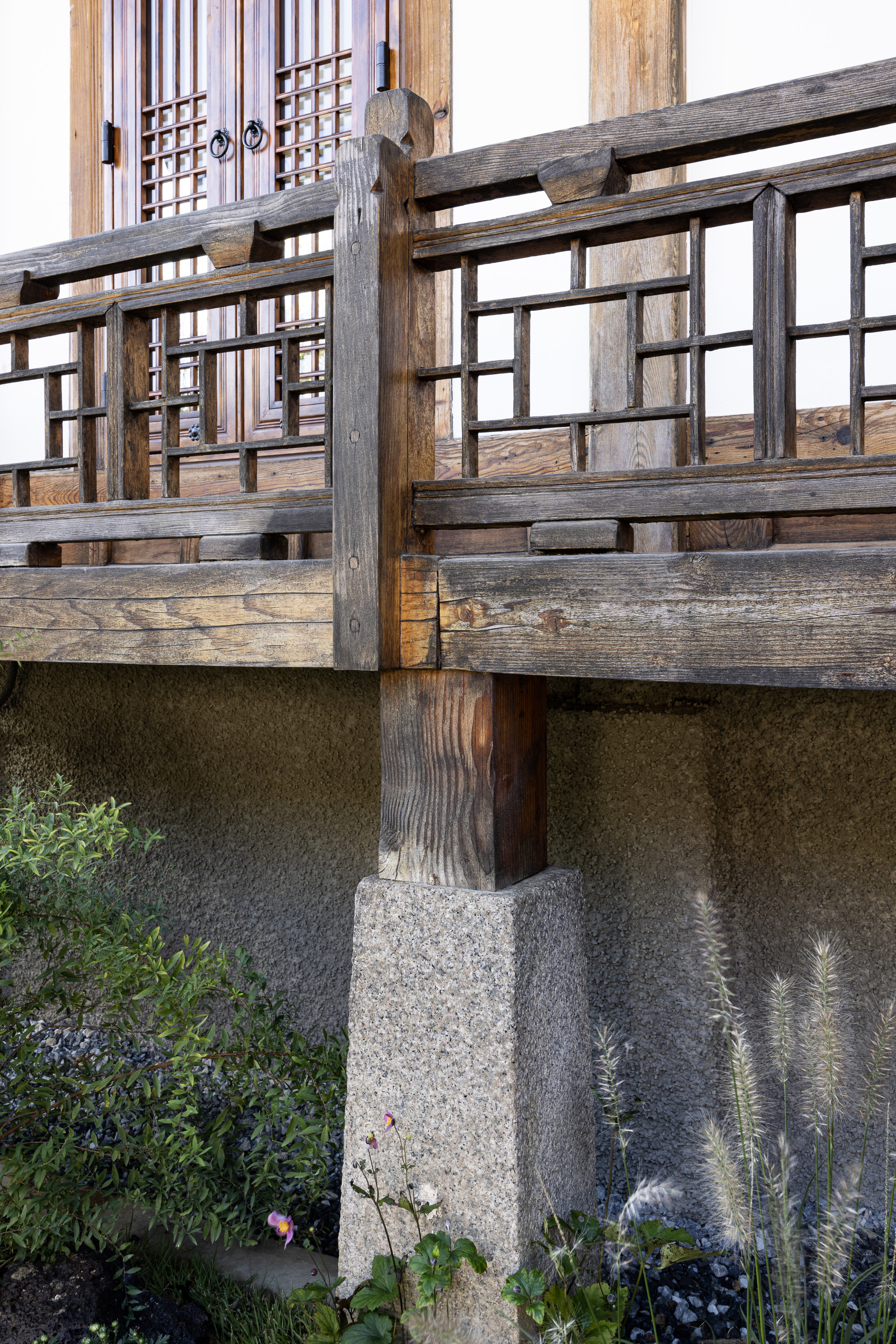 Timber balustrade on a stone plinth beside a planted bed with grasses and shrubs
