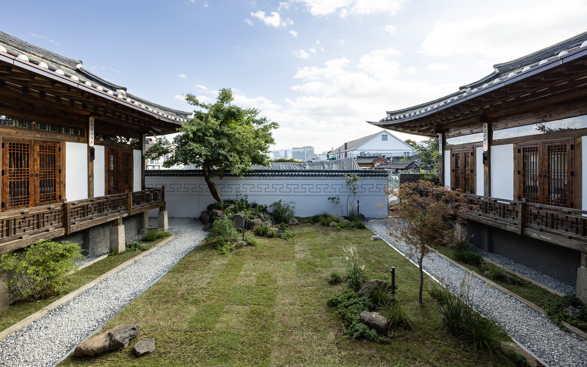 Central courtyard garden with gravel paths between two timber-framed pavilions under a cloudy sky